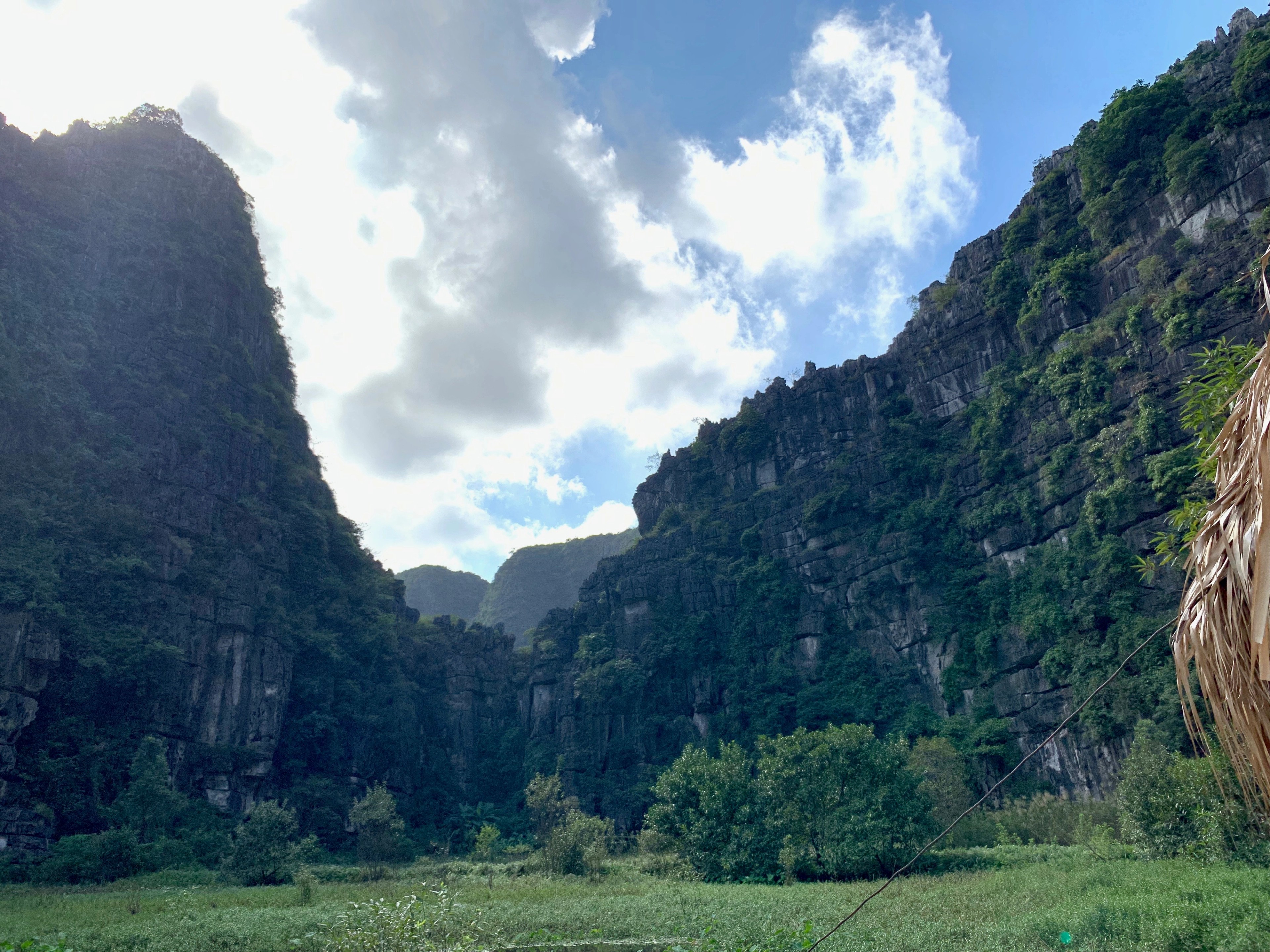 Steep limestone mountains rise around a river beneath a cloudy sky.