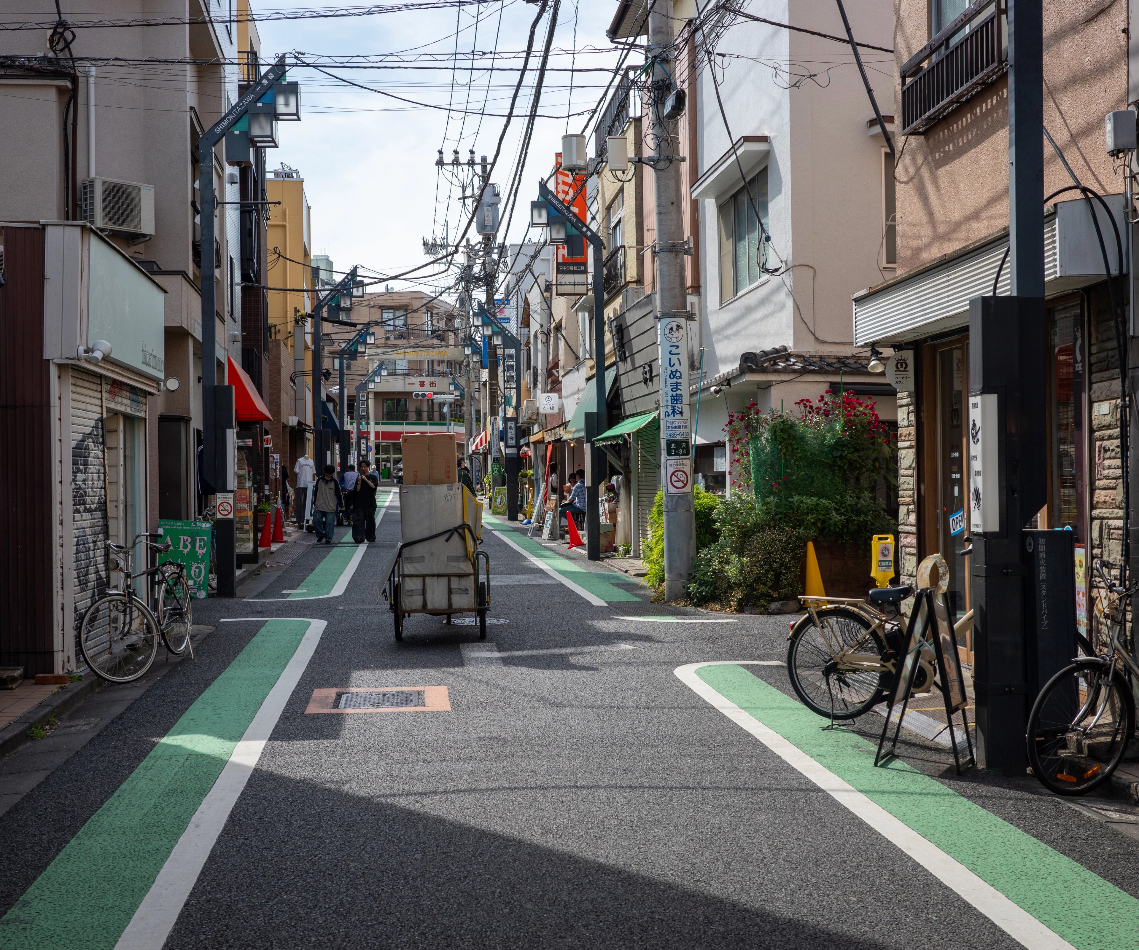A bicycle stands on a narrow urban street beneath overhead cables.