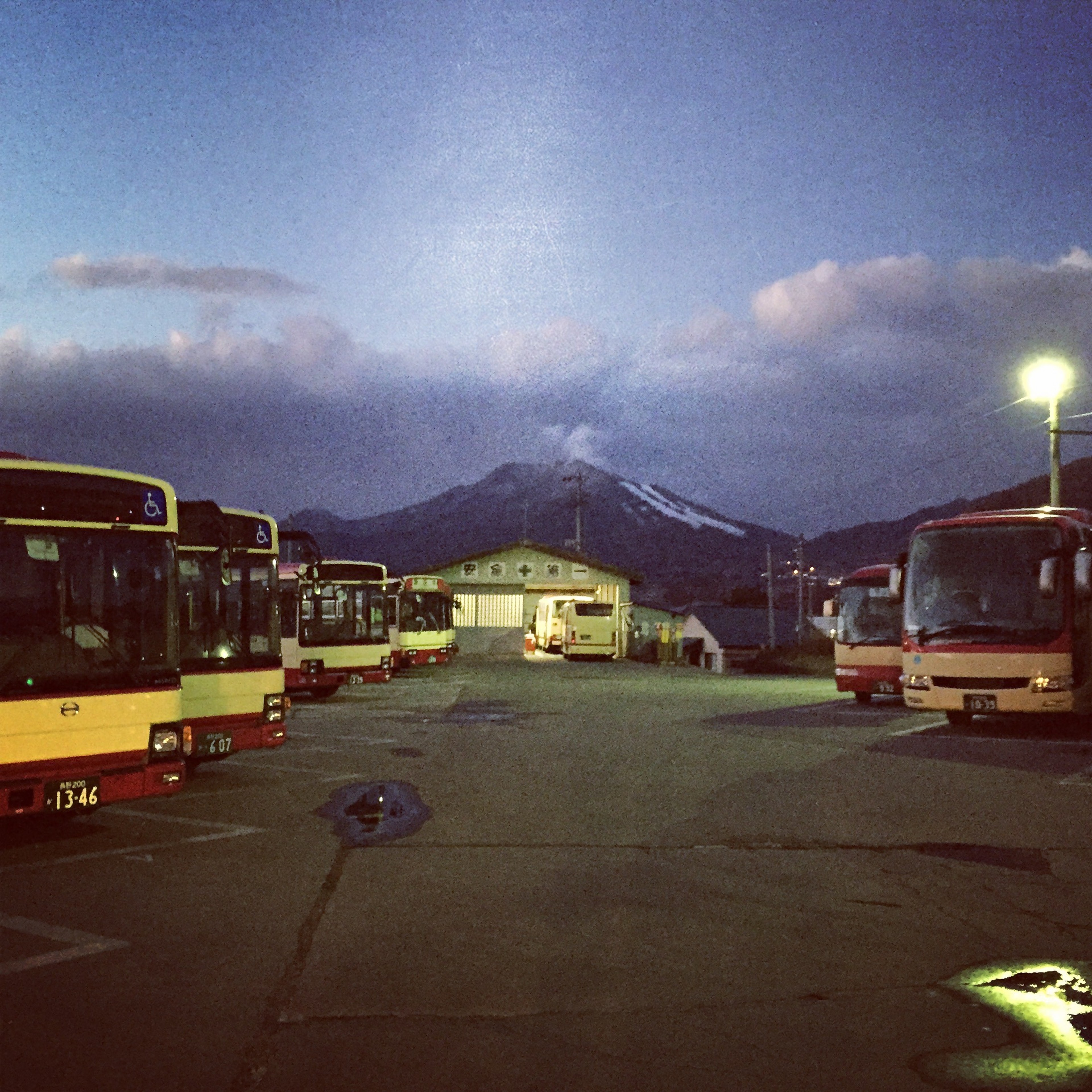 Buses are parked beneath a mountain at dusk.