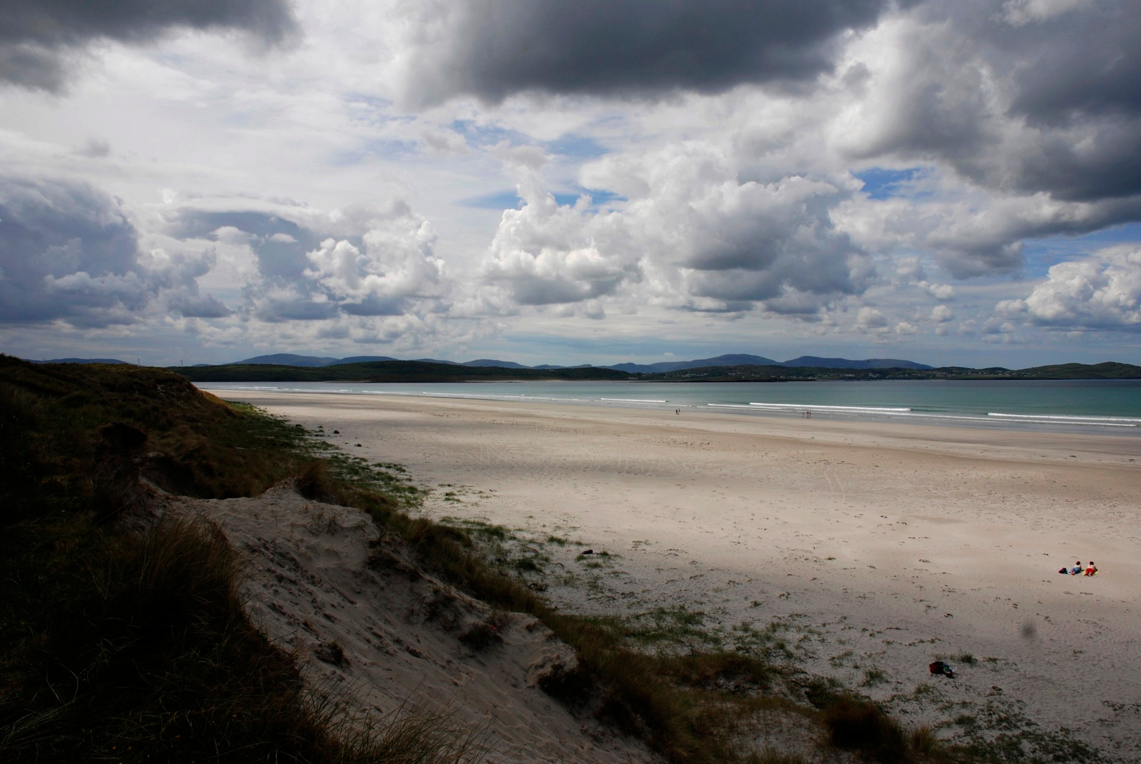 A quiet sandy beach curves along the sea under a sky filled with clouds.