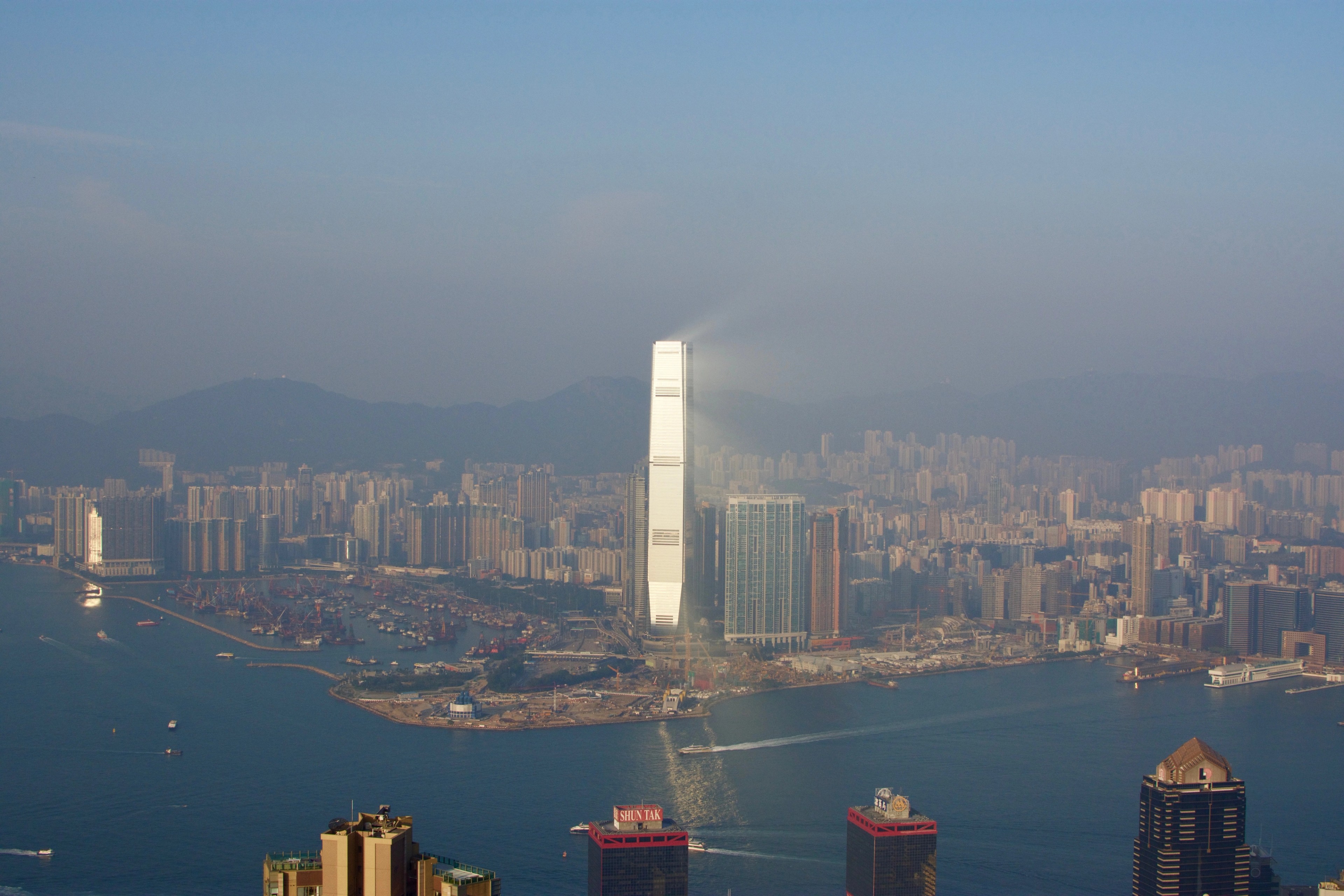 The harbor and a cluster of skyscrapers are seen from a high overlook.