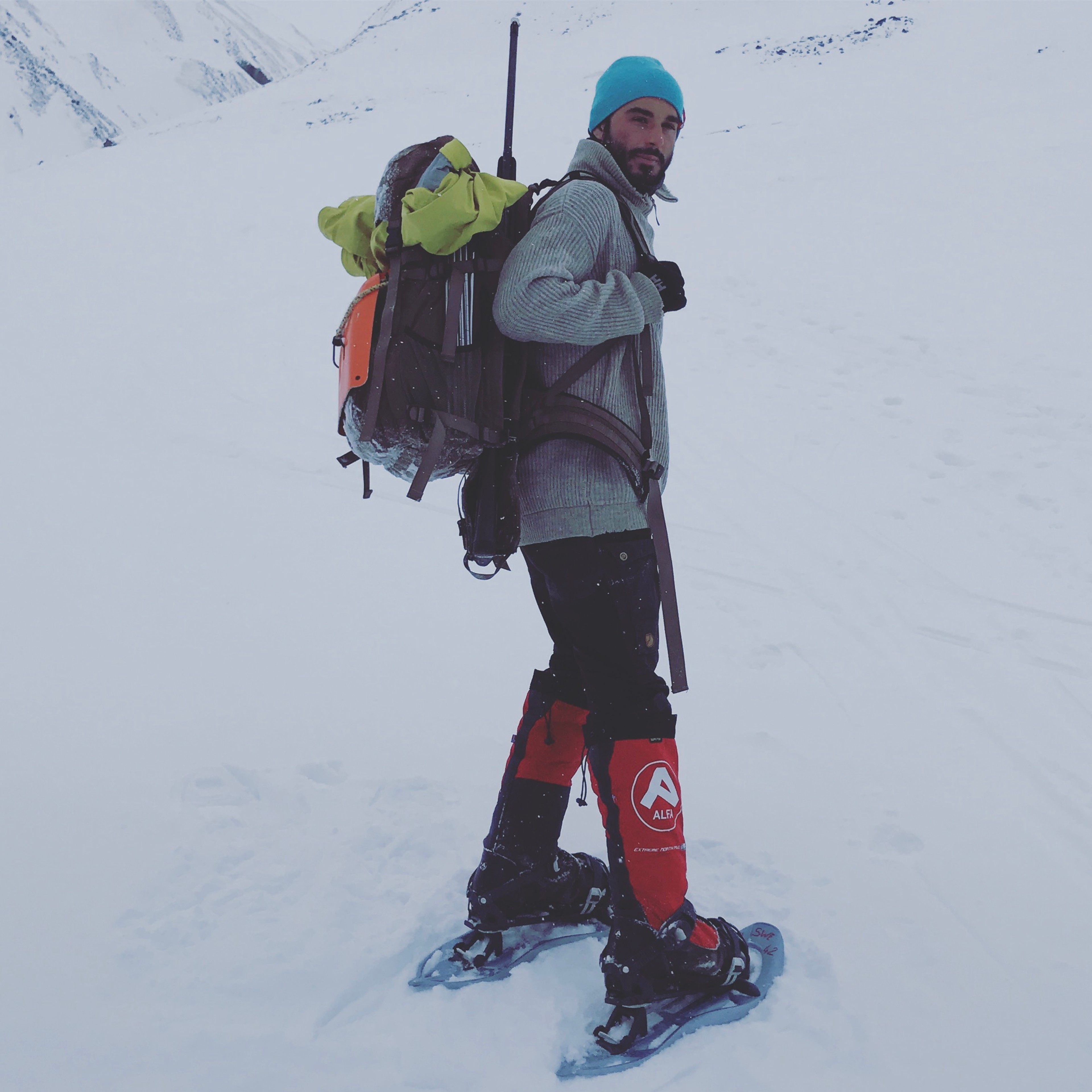 A hiker in snowshoes carries a backpack across the snow.