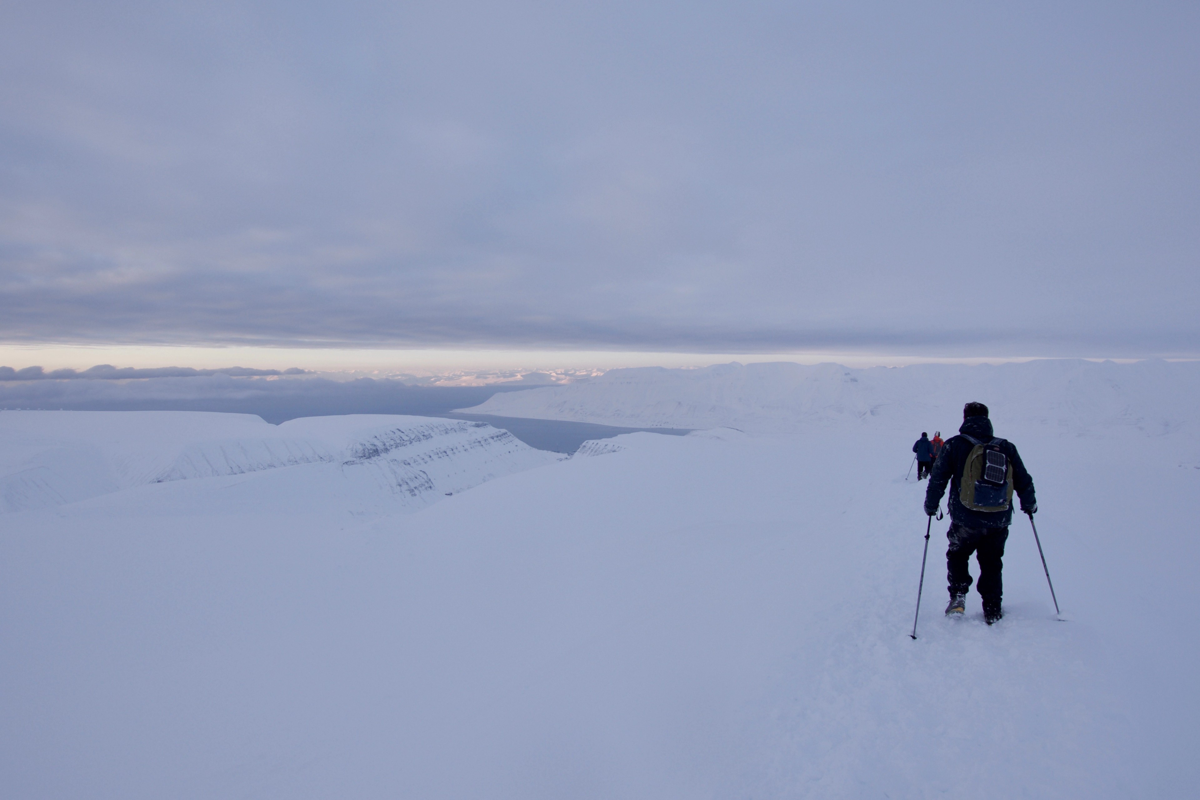 A lone hiker crosses a broad snowy landscape.