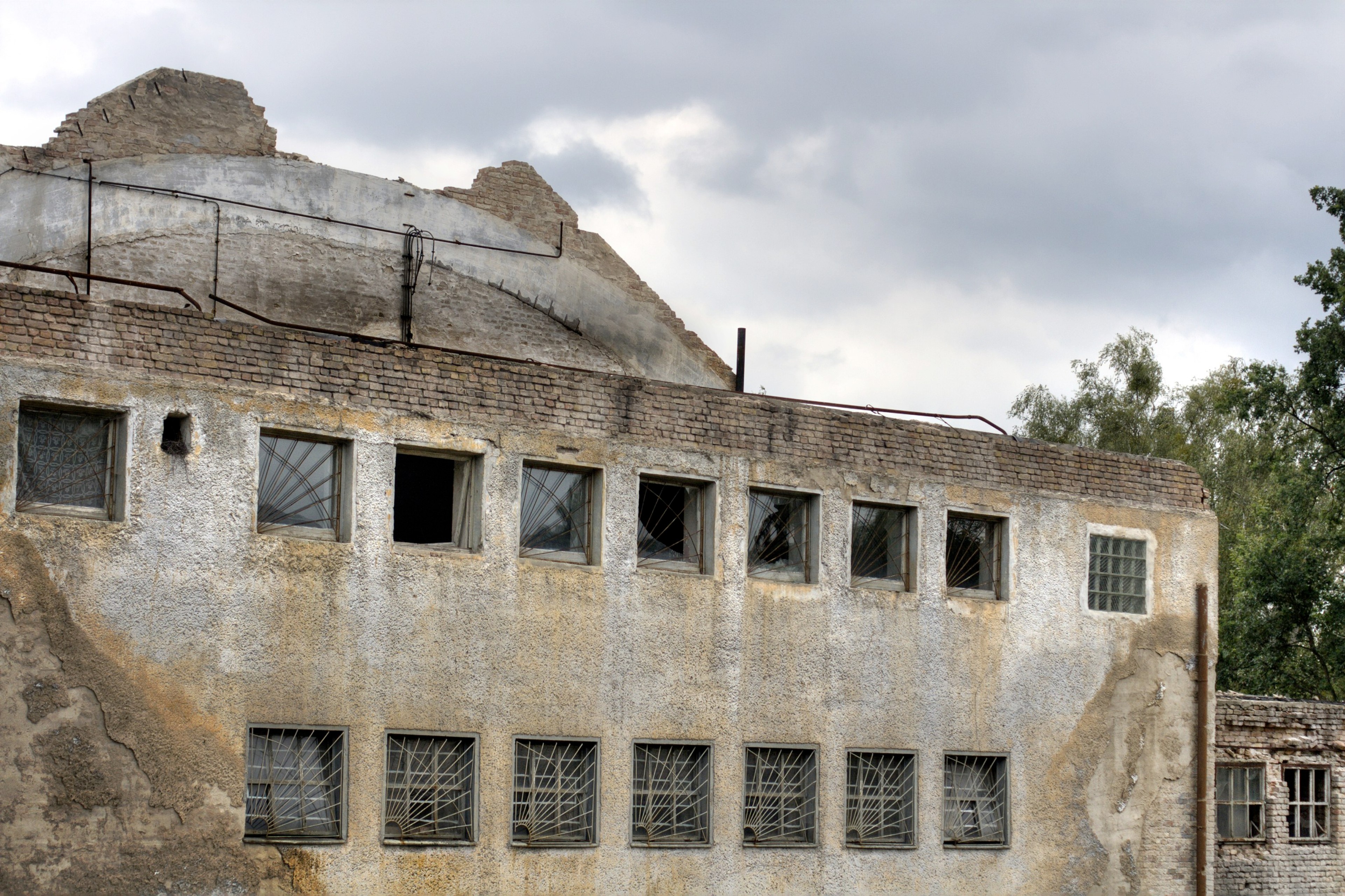 A worn stone building has rows of rectangular windows beneath a damaged roofline.