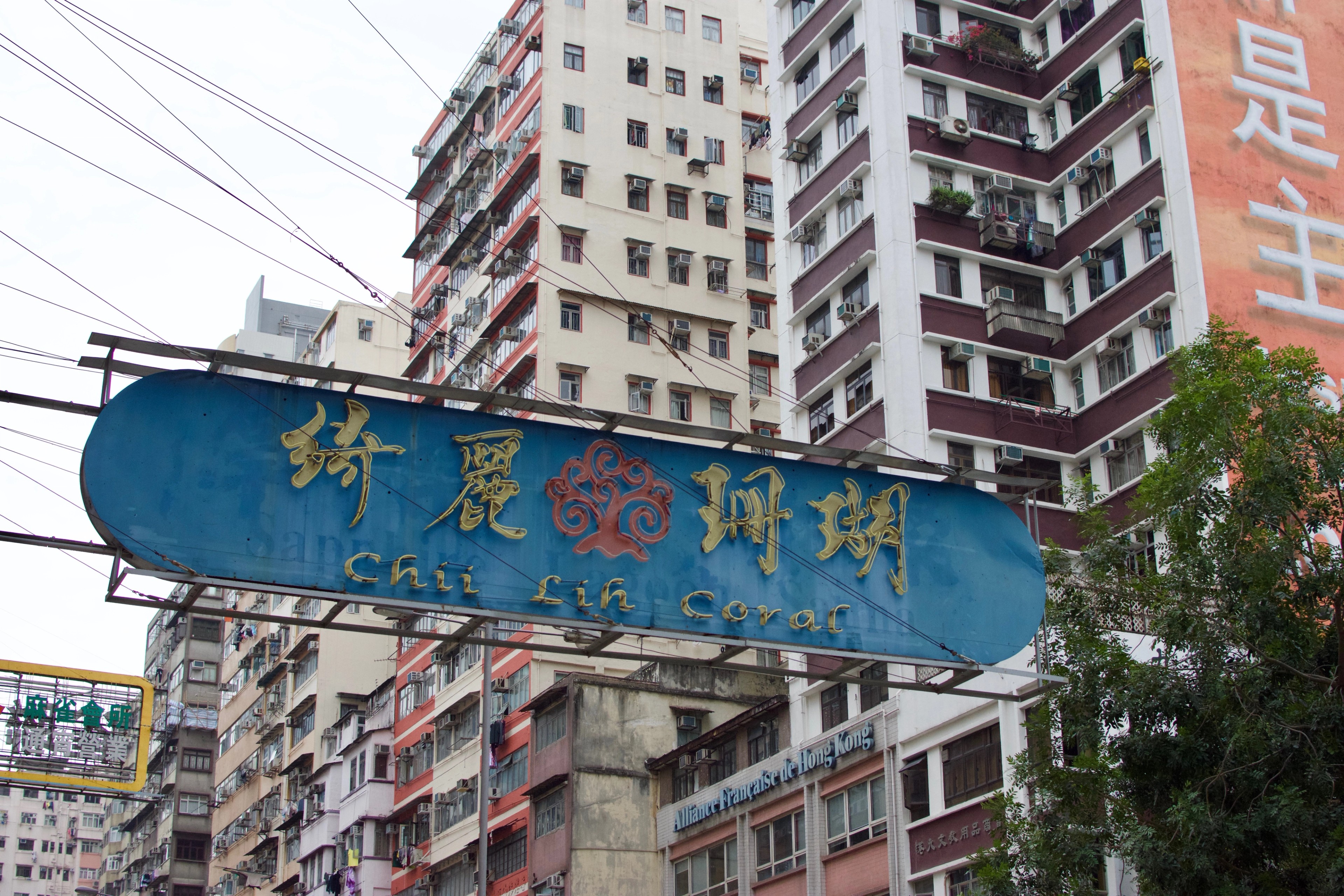 A blue Chinese-language street sign hangs above a daytime street lined with high-rise buildings.