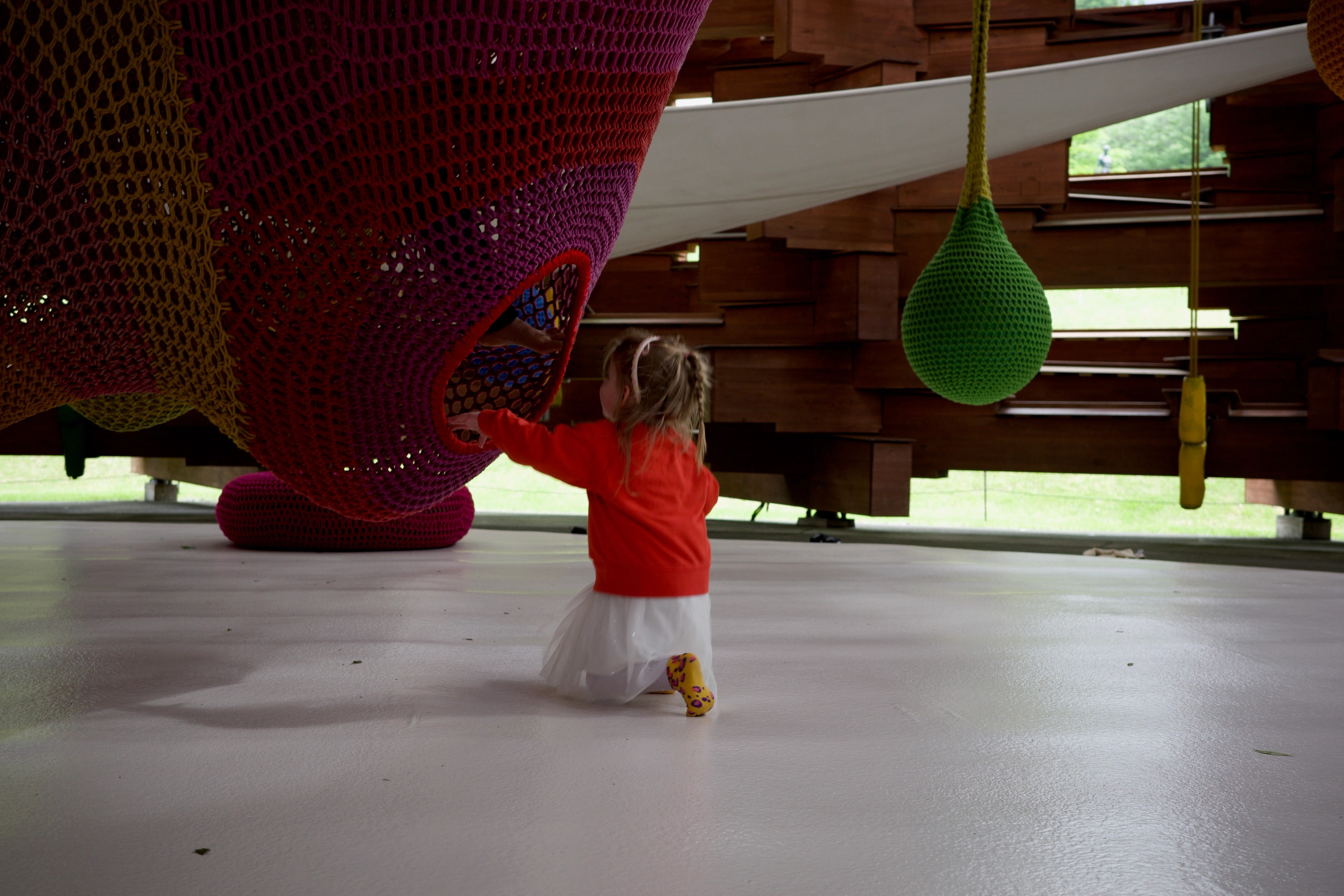 A child reaches toward a red curved installation beneath a wooden ceiling.