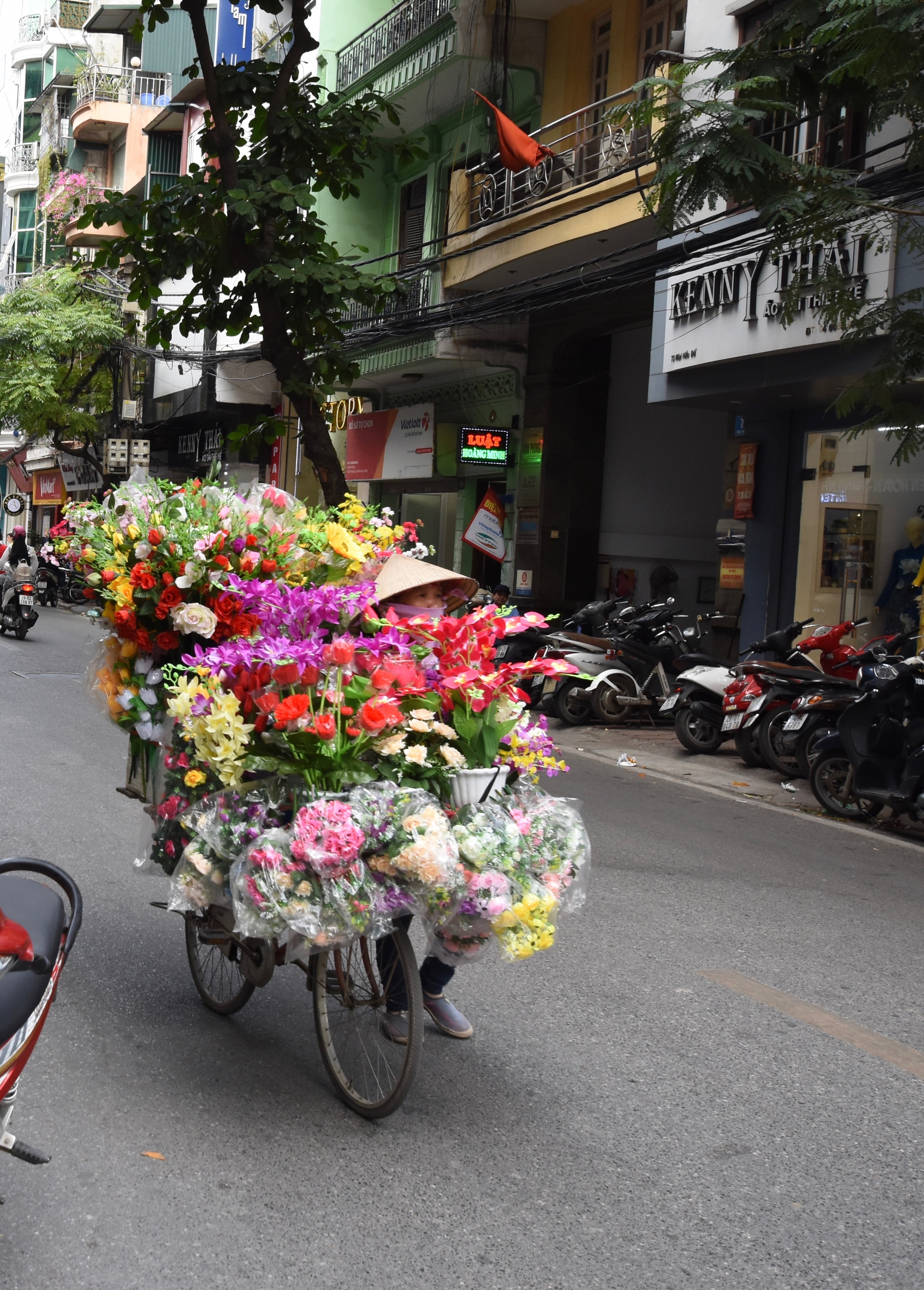 A flower seller rides a bicycle loaded with bright bouquets.