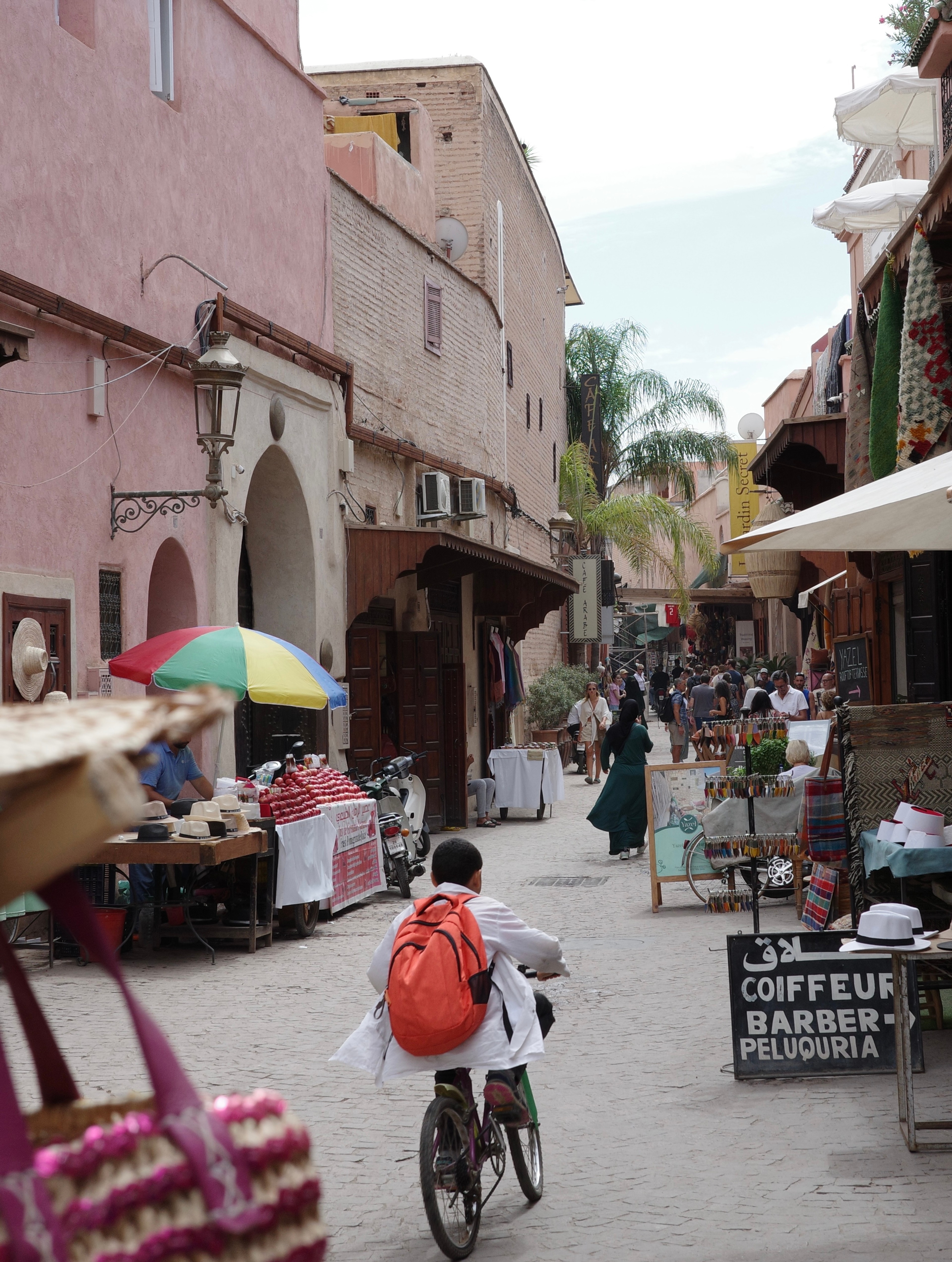 Pedestrians and a cyclist pass through a busy narrow street market.