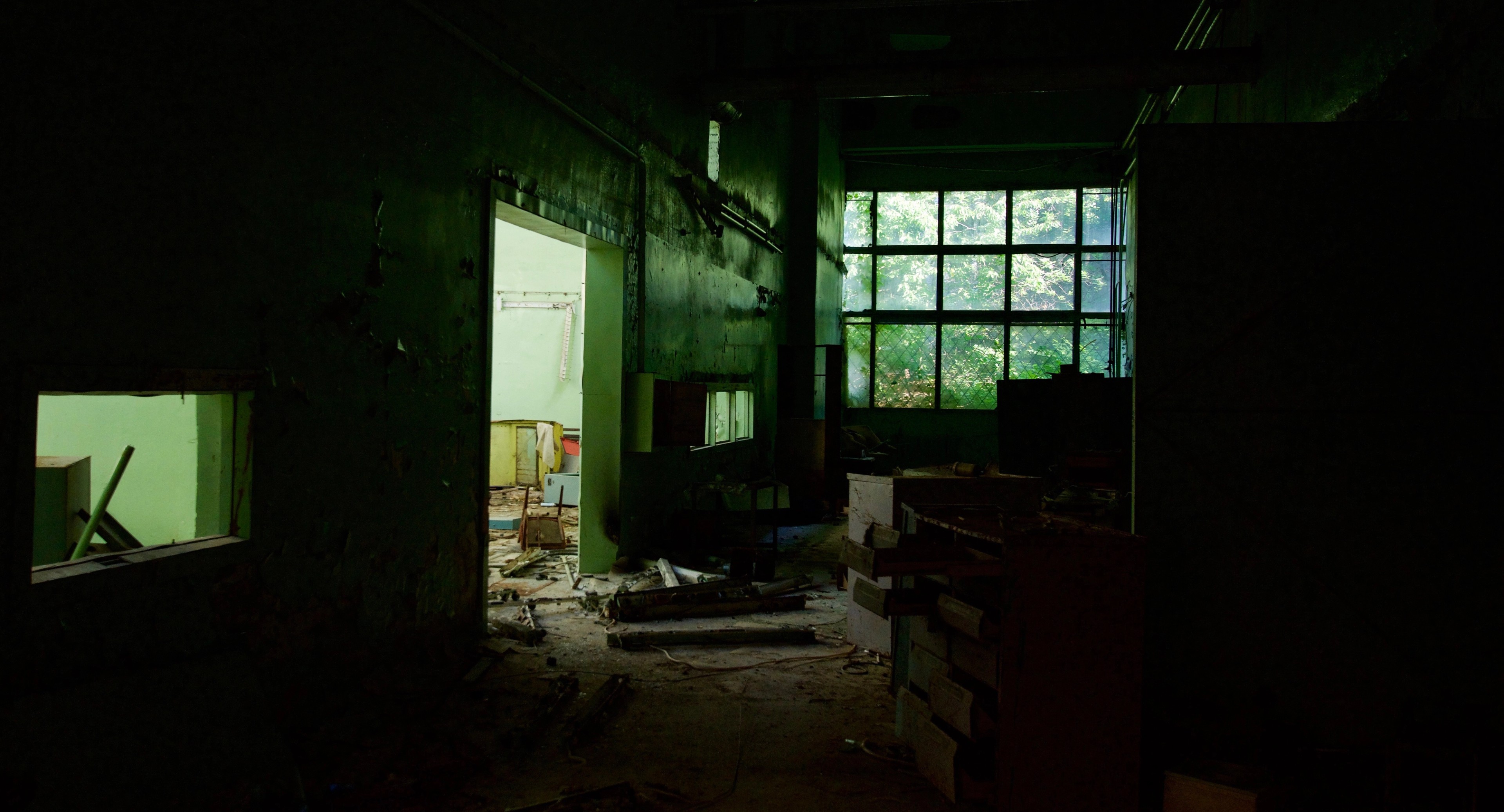 A dark classroom full of debris seen through a doorway.