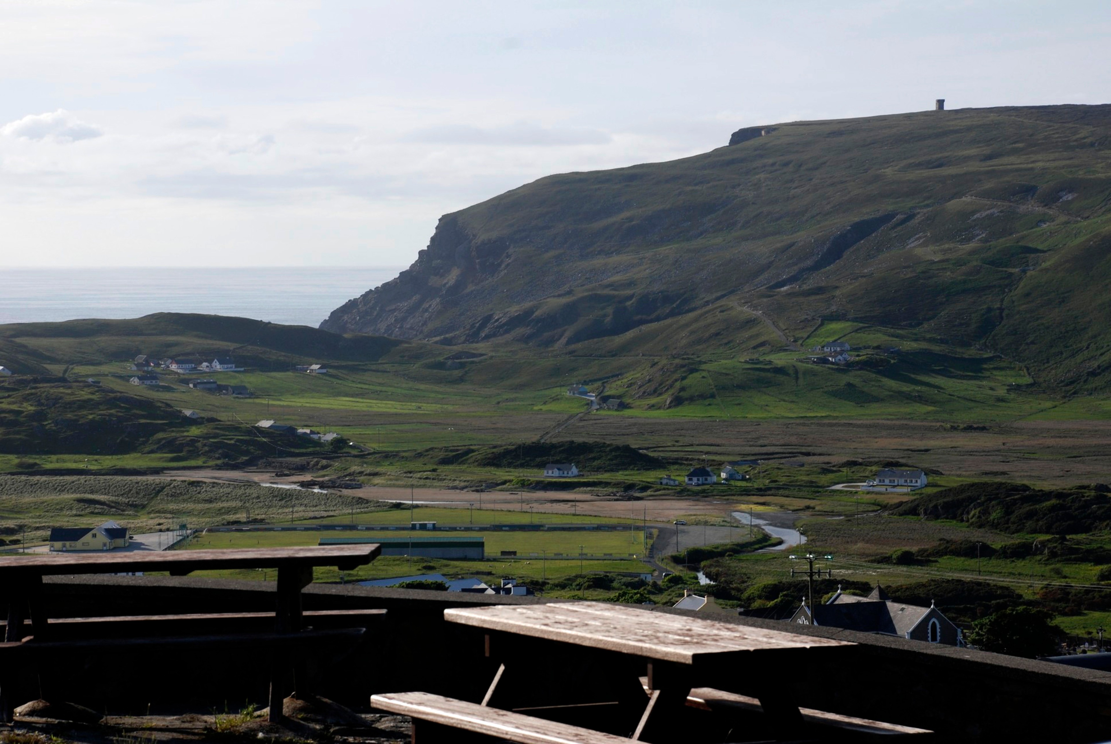 A broad green valley and mountains seen from a roadside viewpoint.