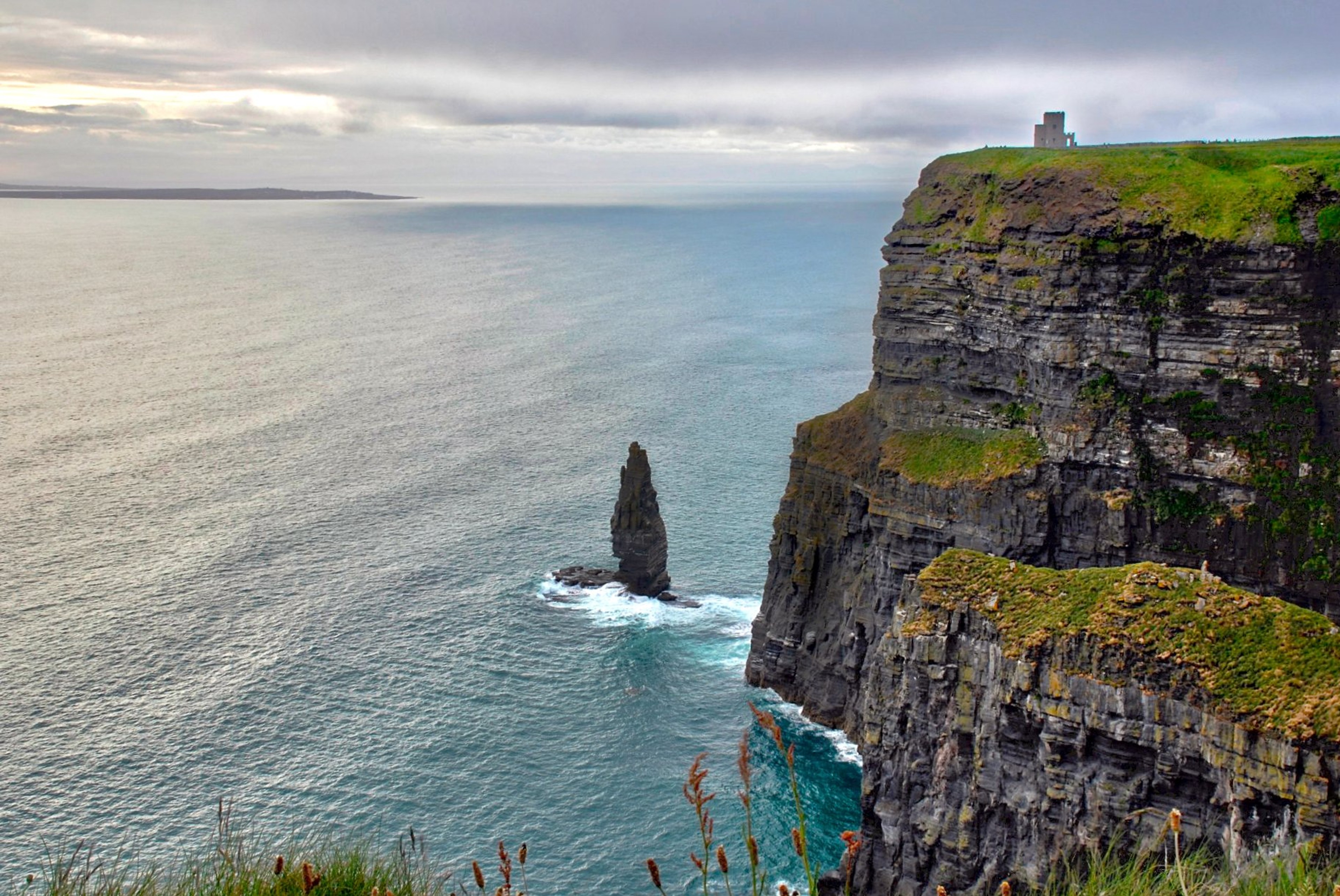 The Cliffs of Moher rise above the Atlantic as waves break around a tall rock stack.