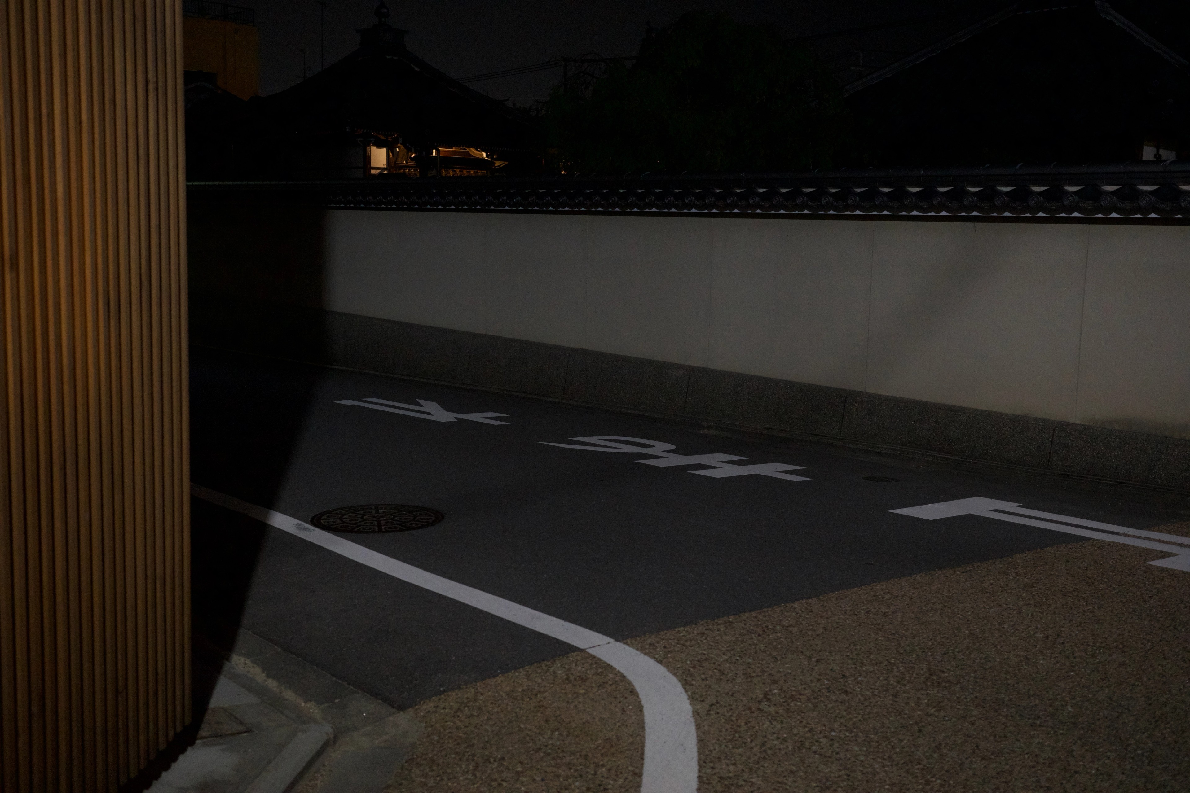 A curved road runs beside a white wall at night.