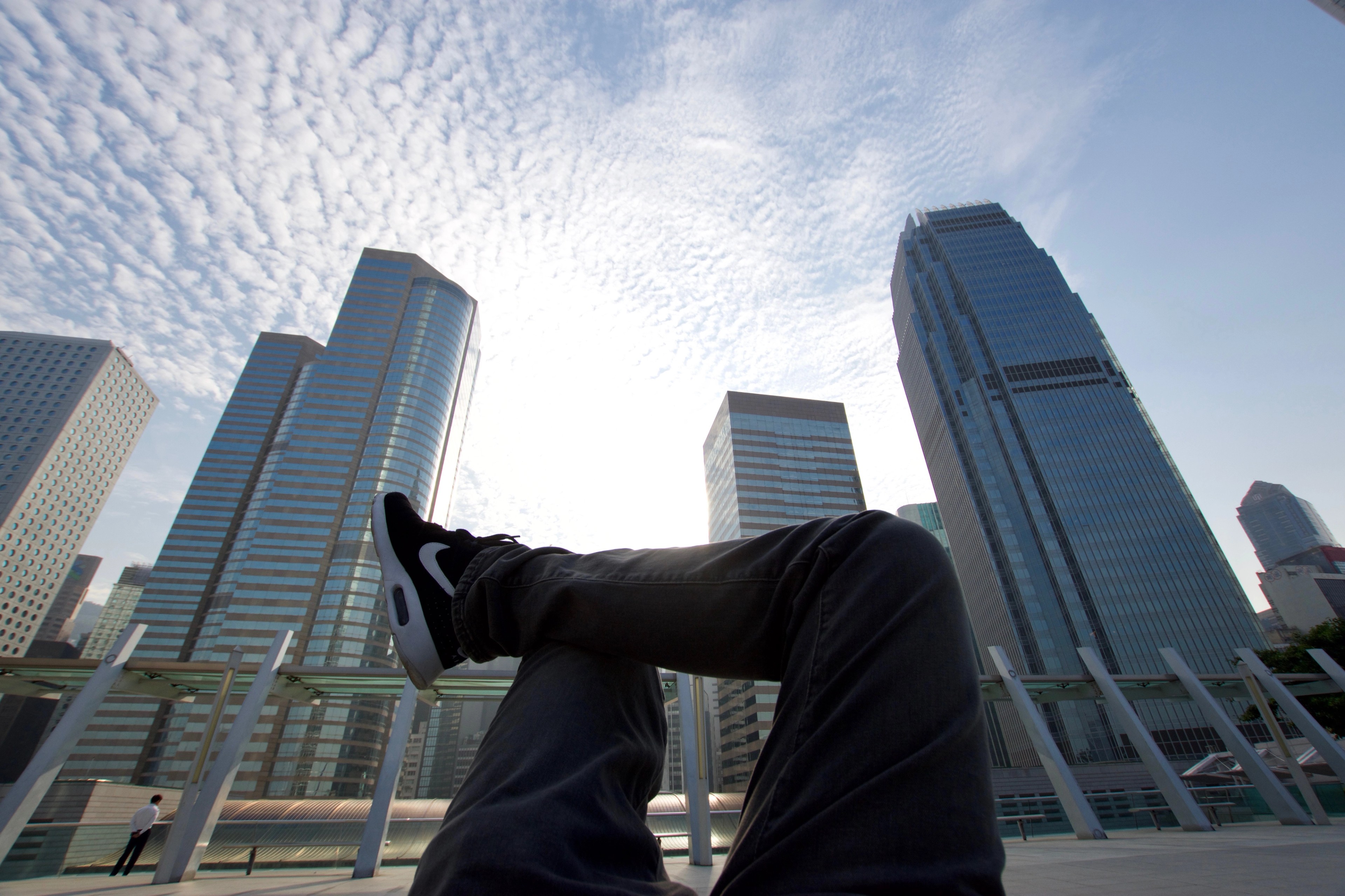 A person’s legs extend toward the sky between surrounding skyscrapers.