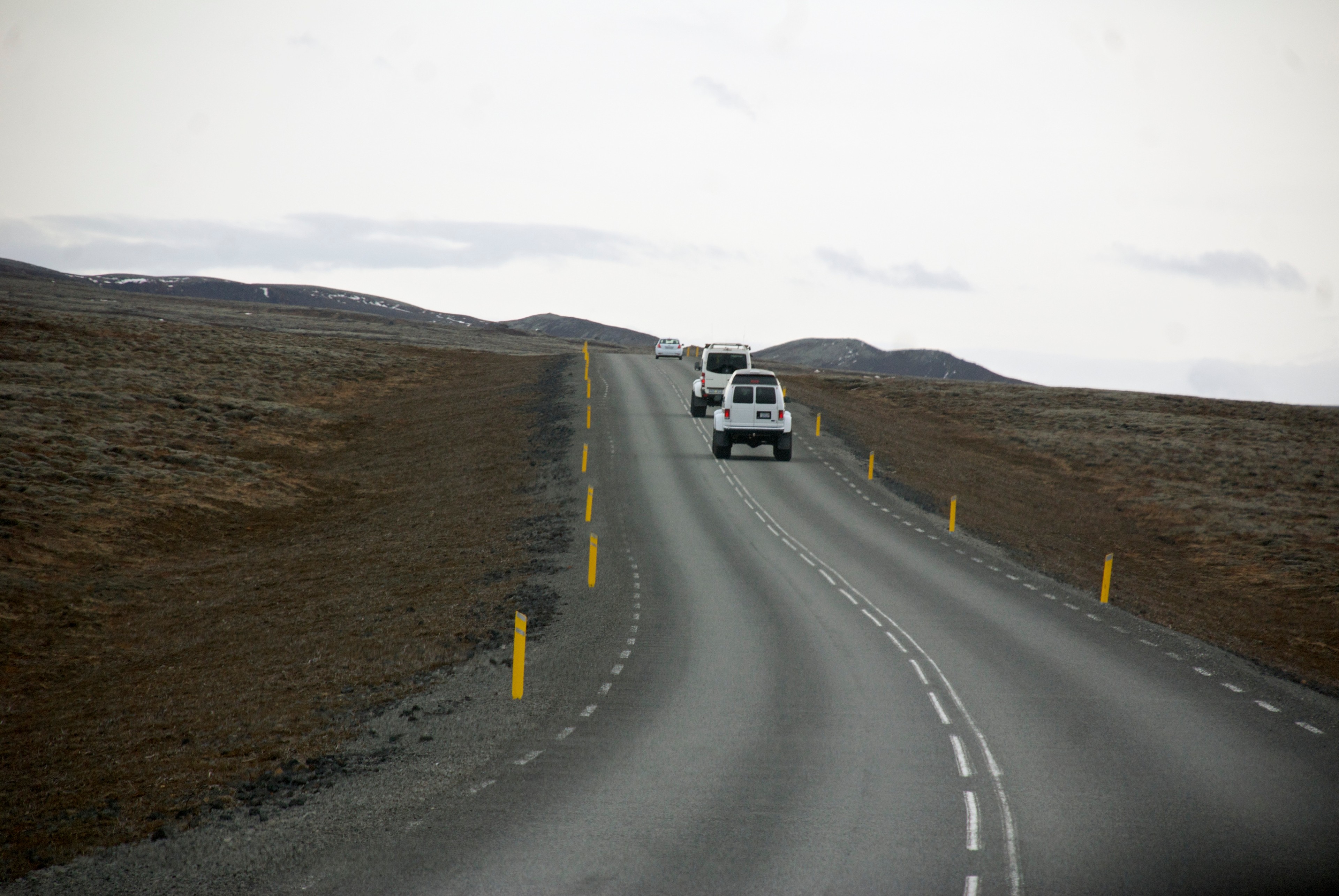 Two vehicles follow a road through a treeless mountain landscape.