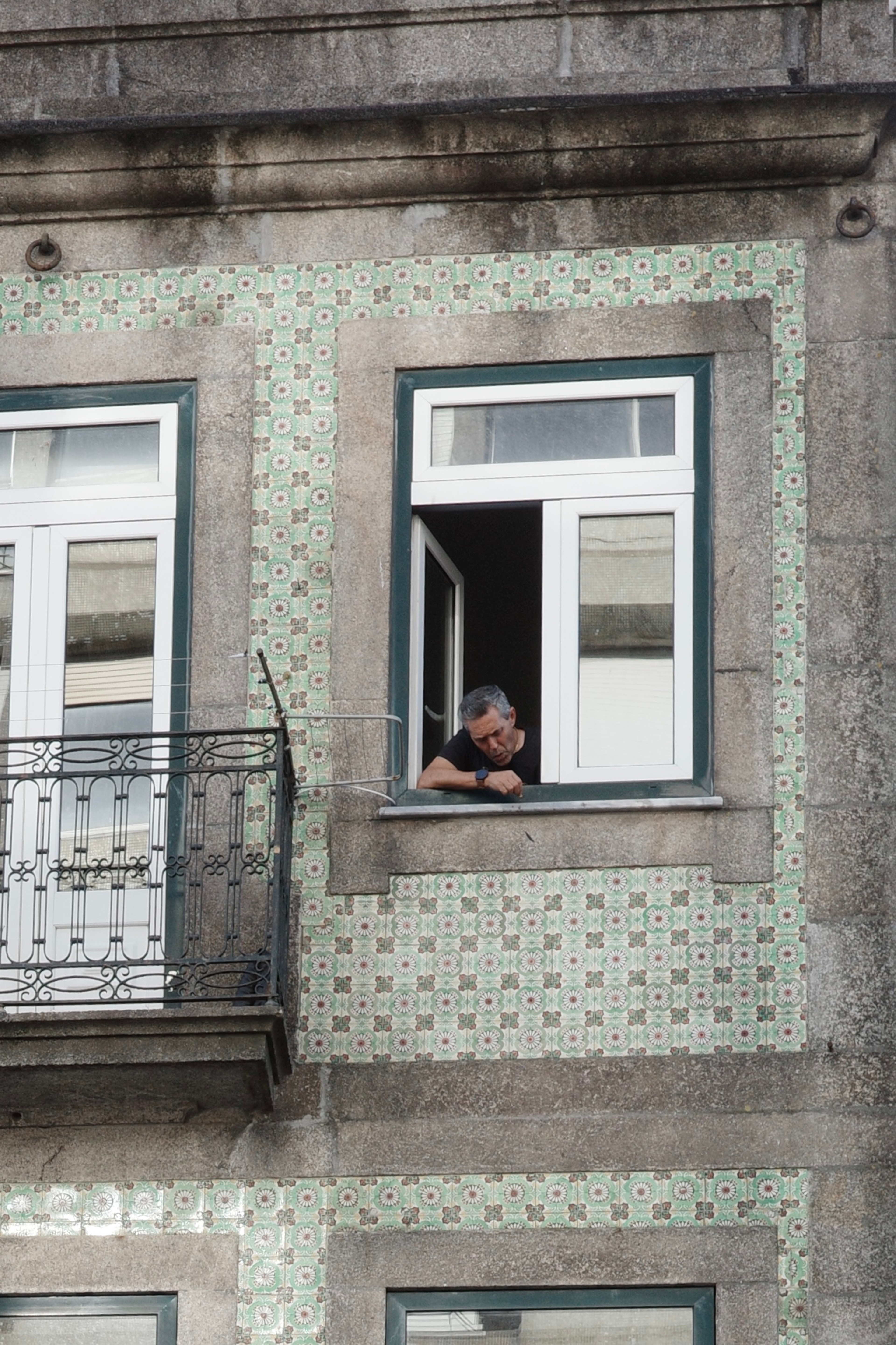 A person looks out from a window above a tiled Porto street façade.