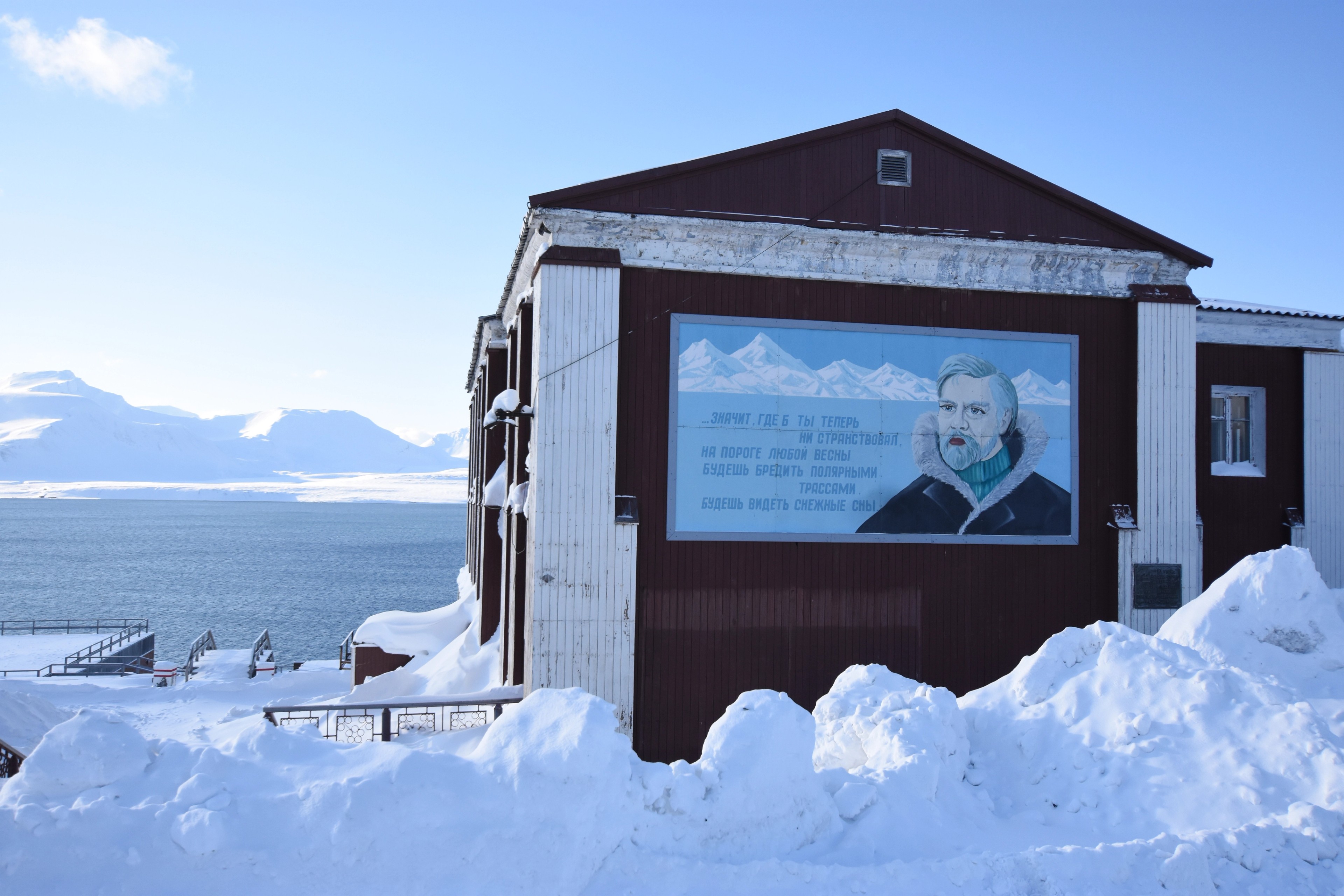 A building bears a large portrait sign beside a snowy road.