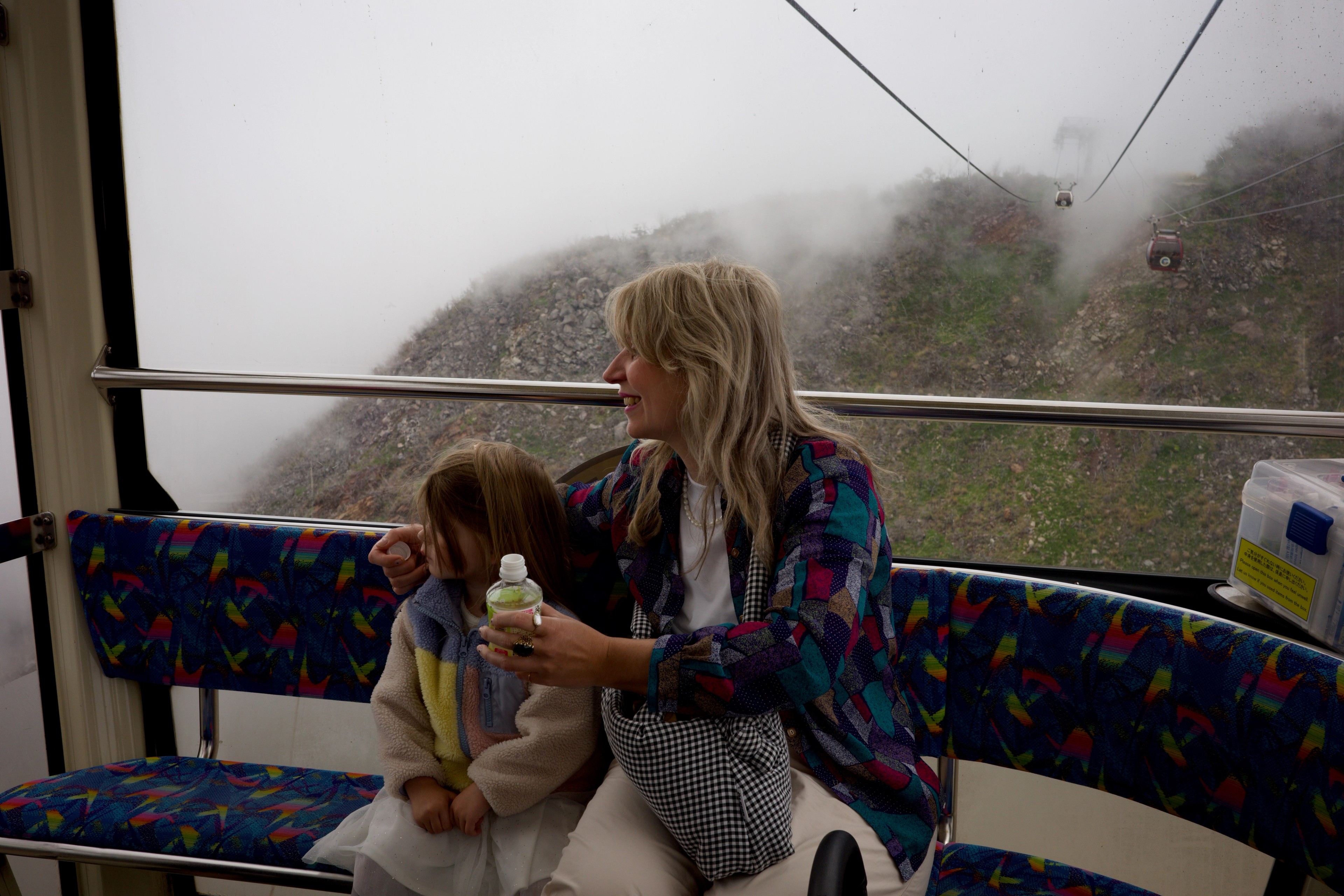 A woman and child ride a cable car through fog.