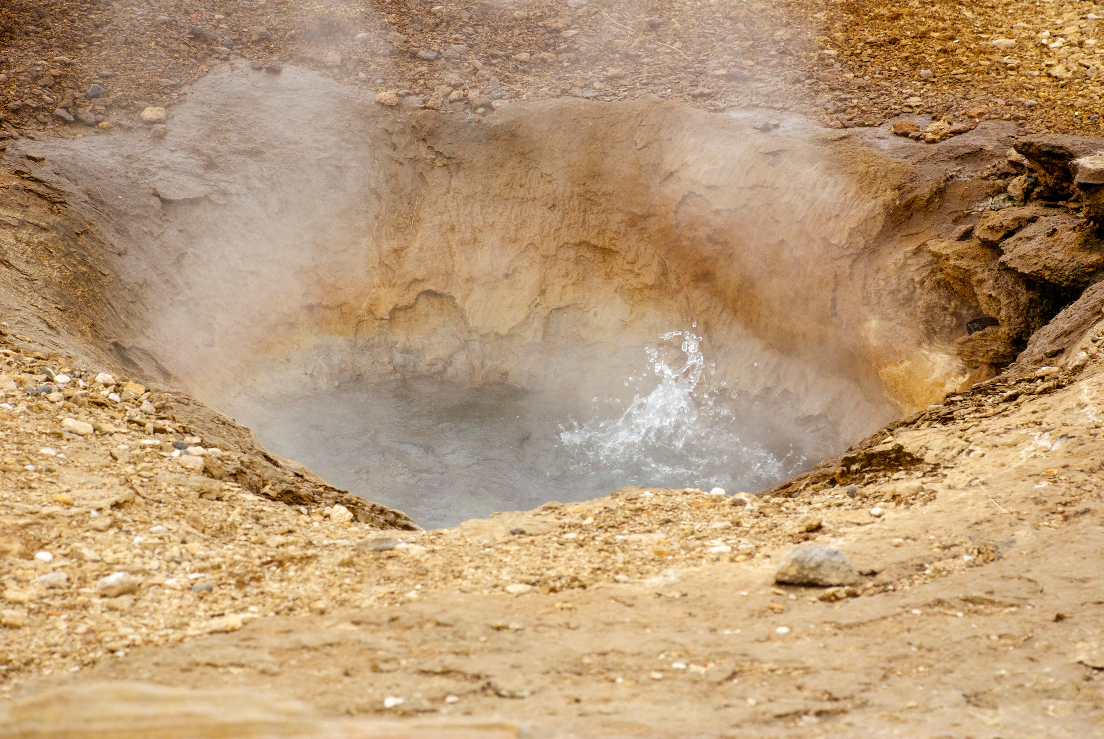 A bubbling geothermal pool steams within a rough ochre-colored field.