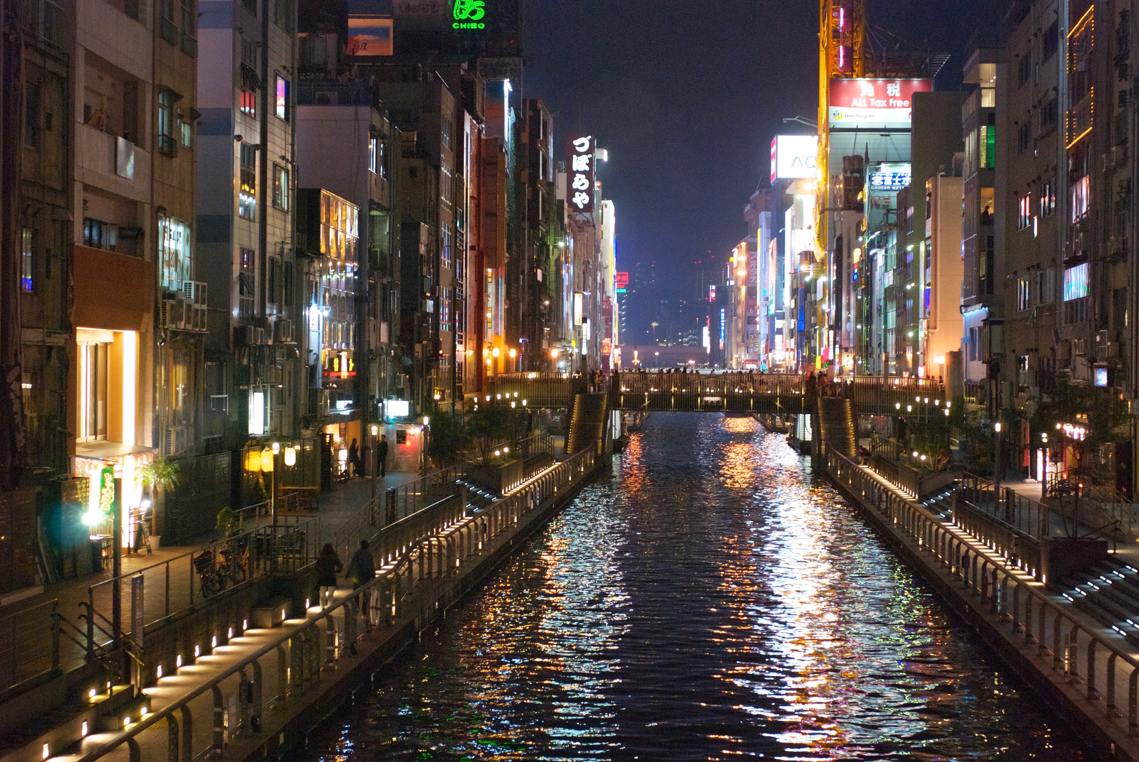 A canal reflects neon signs and buildings at night.
