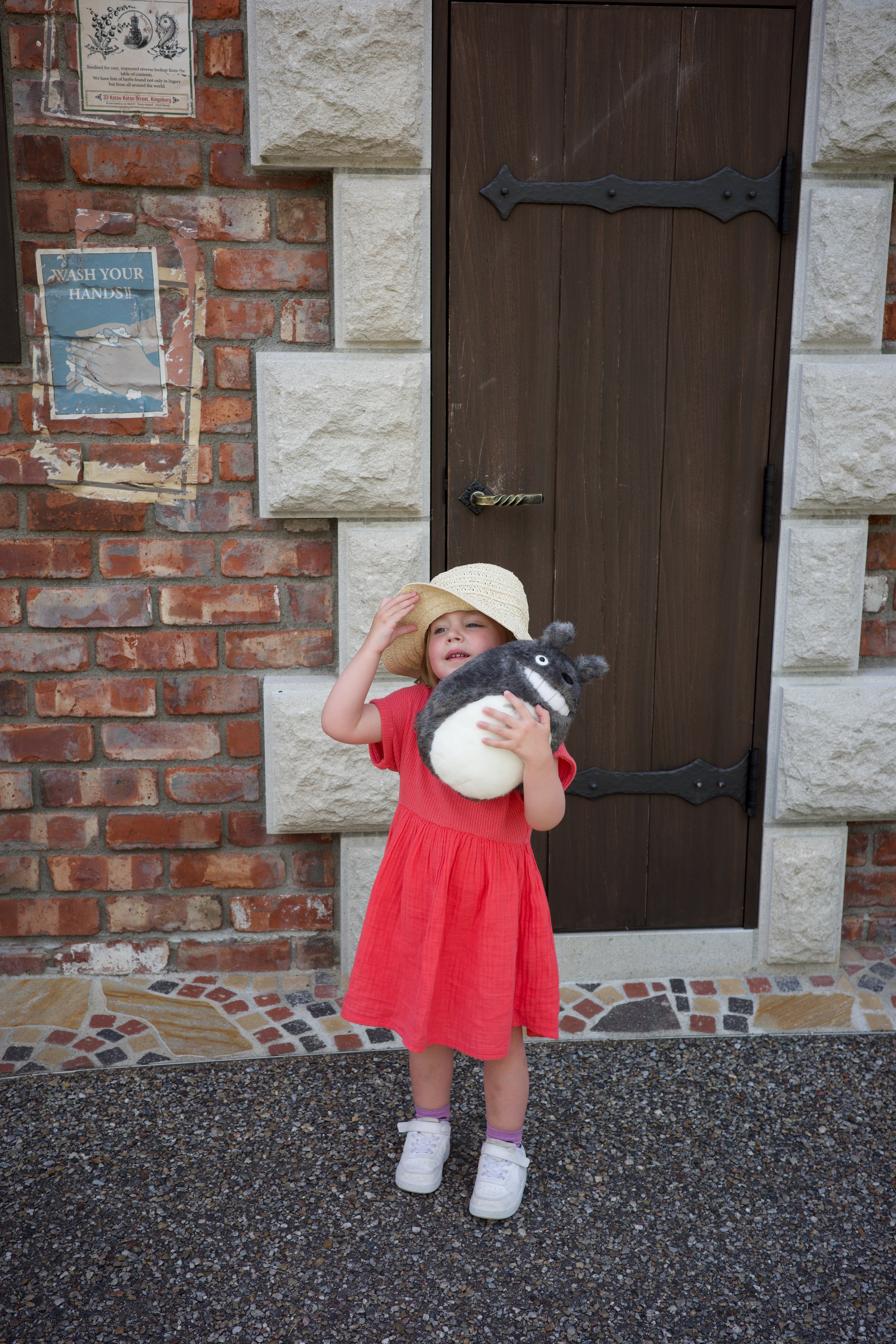 A child in a red dress stands in front of a brick wall.