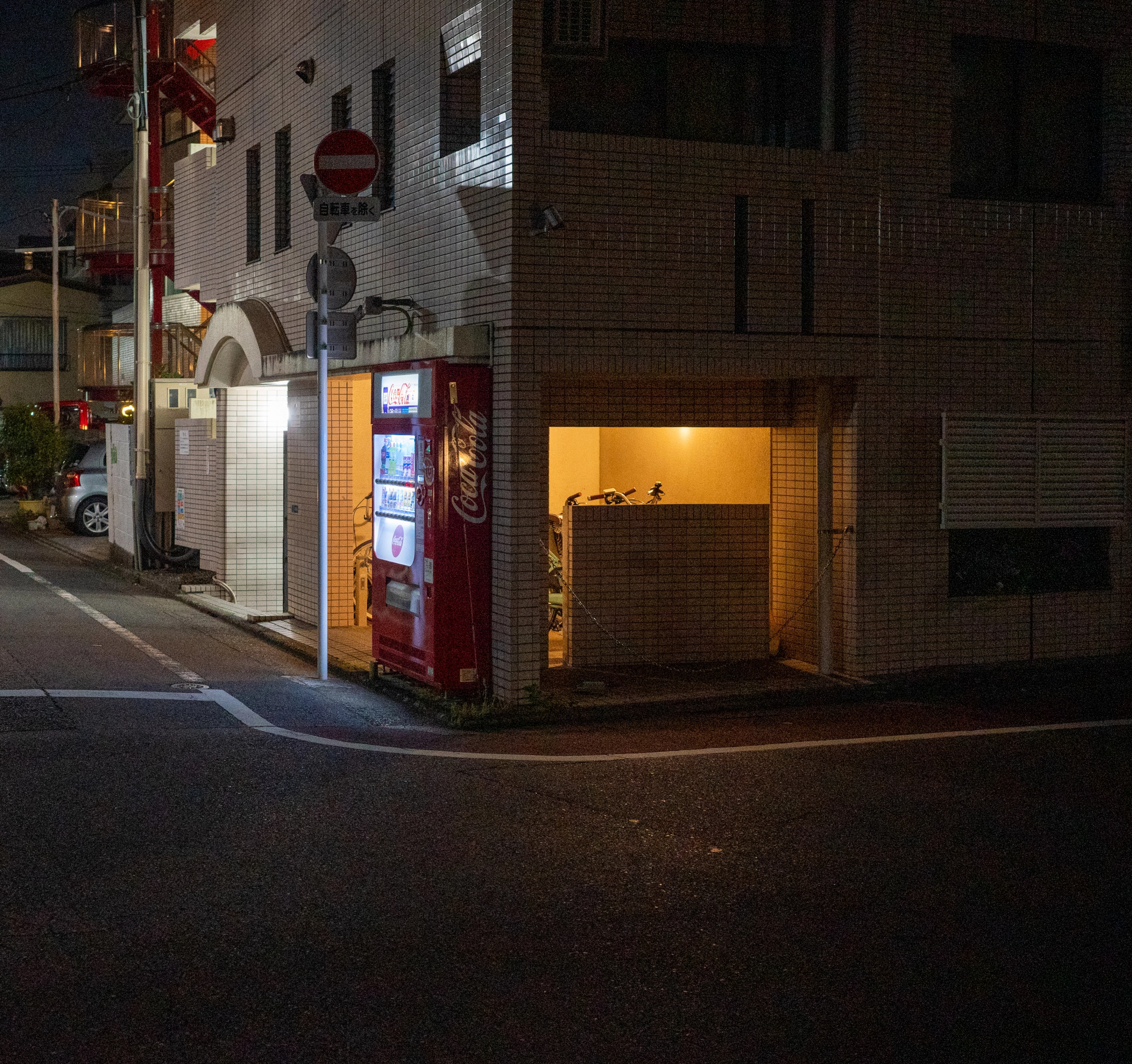 A narrow street with a brightly lit doorway at night.
