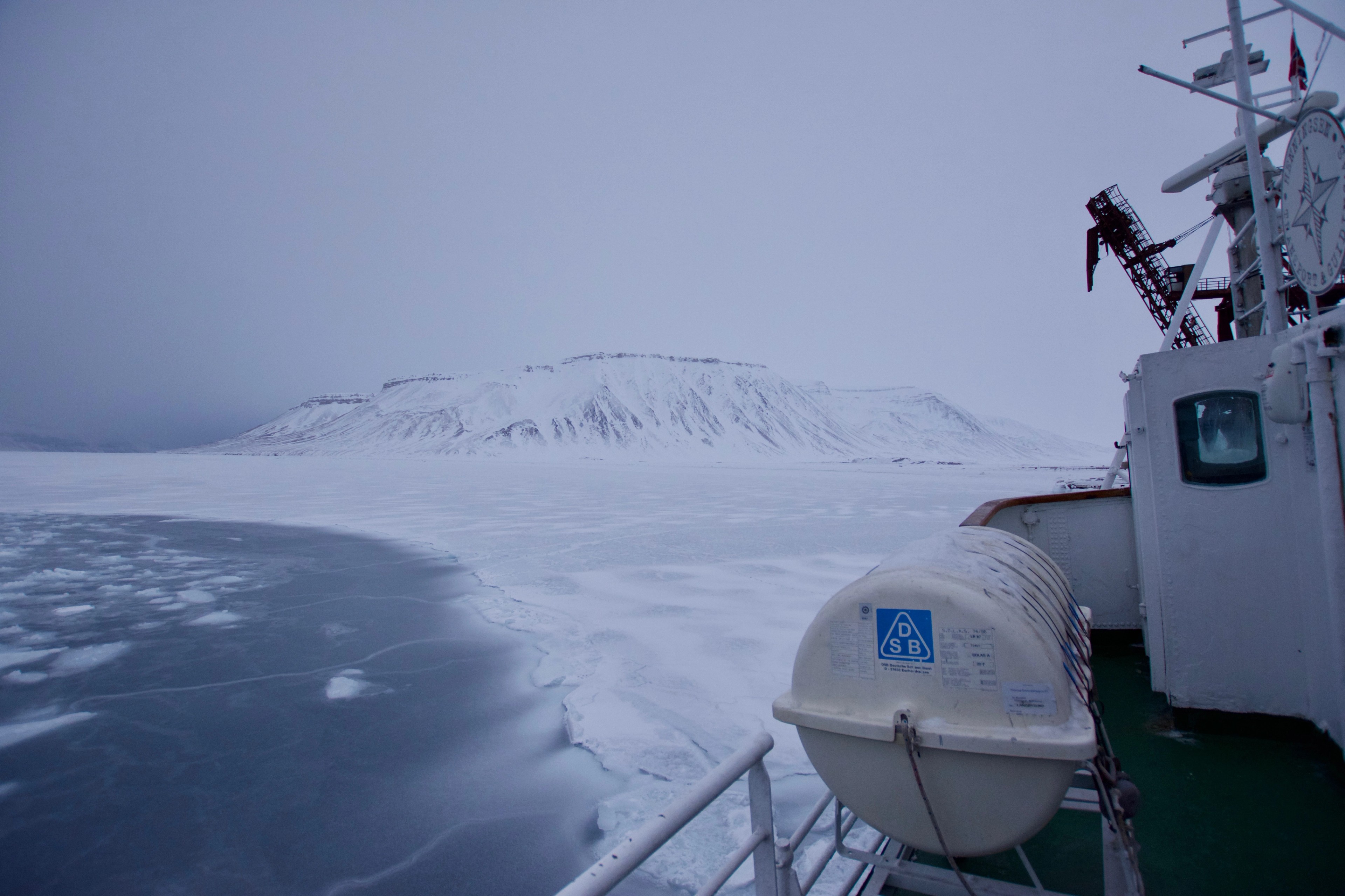 A small boat passes snowy mountains and drifting sea ice.