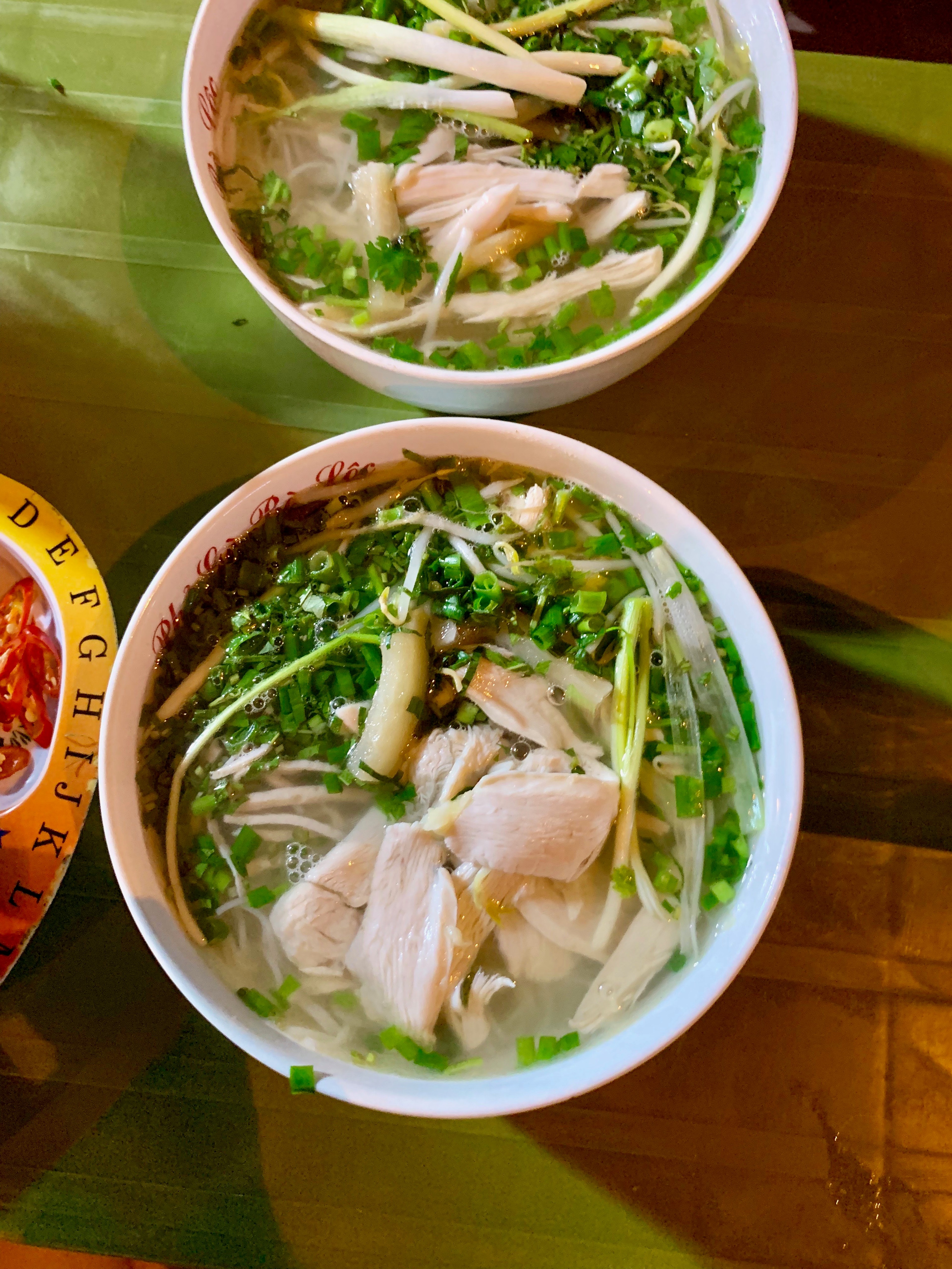 Two bowls of noodle soup sit on a wooden table.