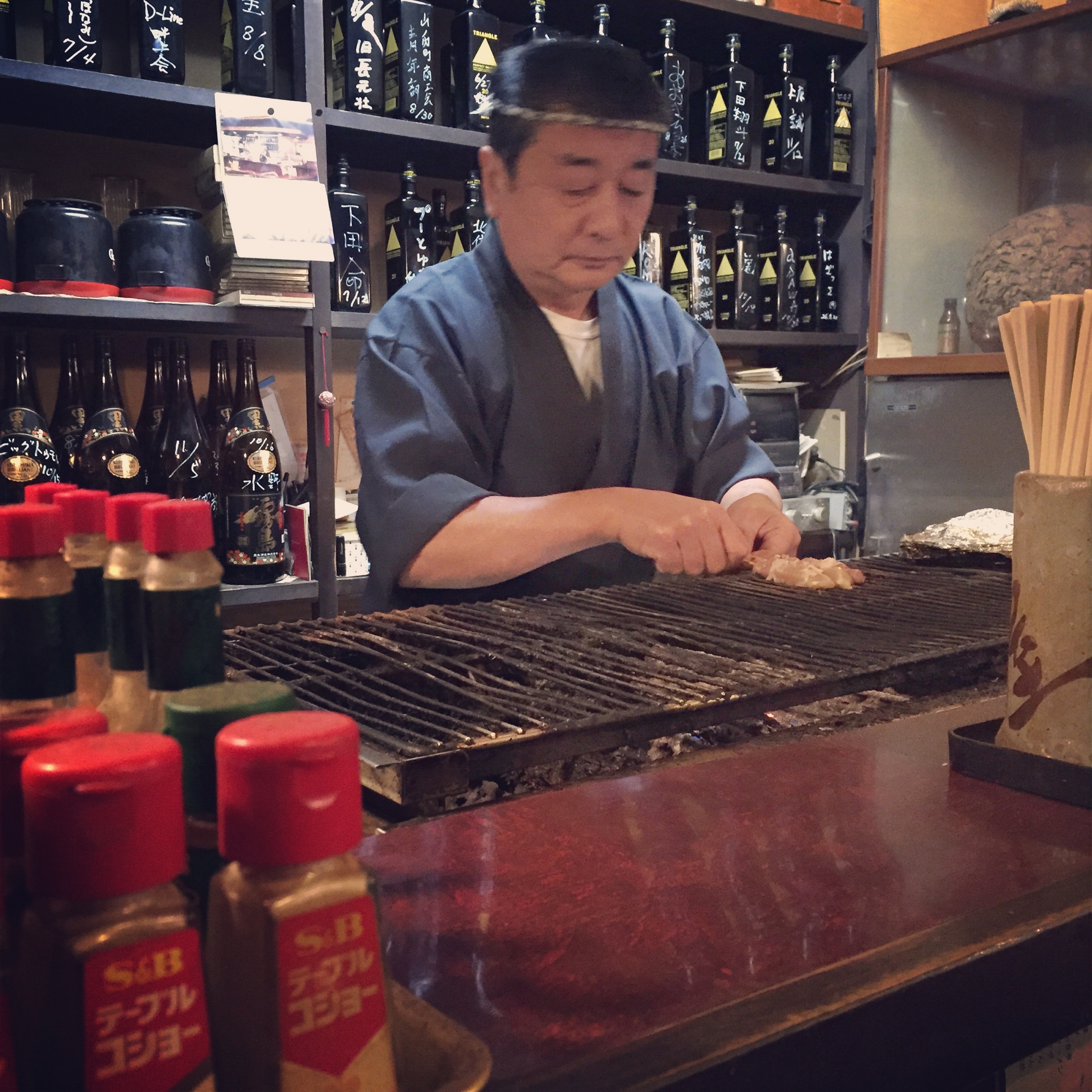A cook prepares food at a counter lined with bottles and containers.