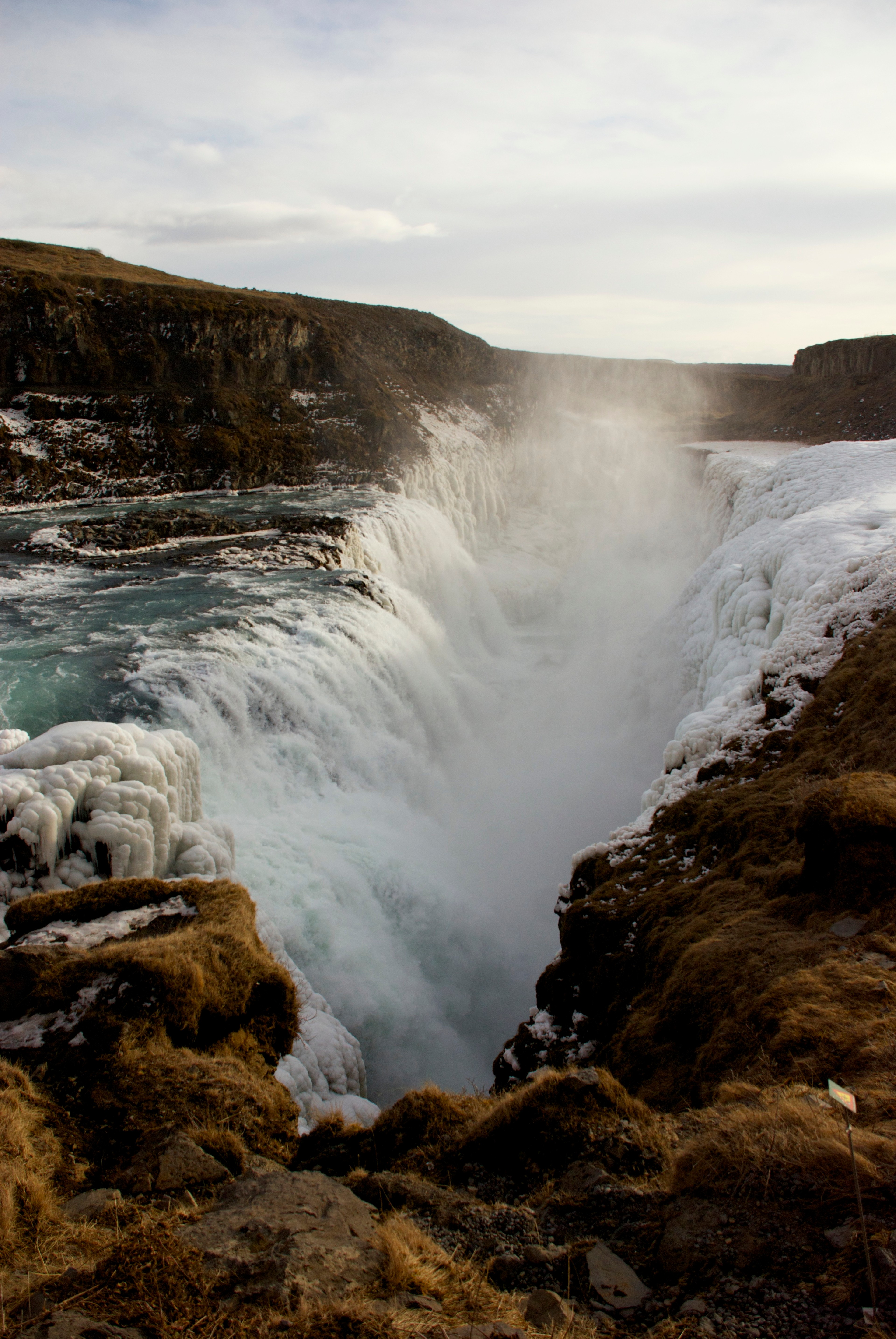 A waterfall drops over dark rocks into a narrow river.