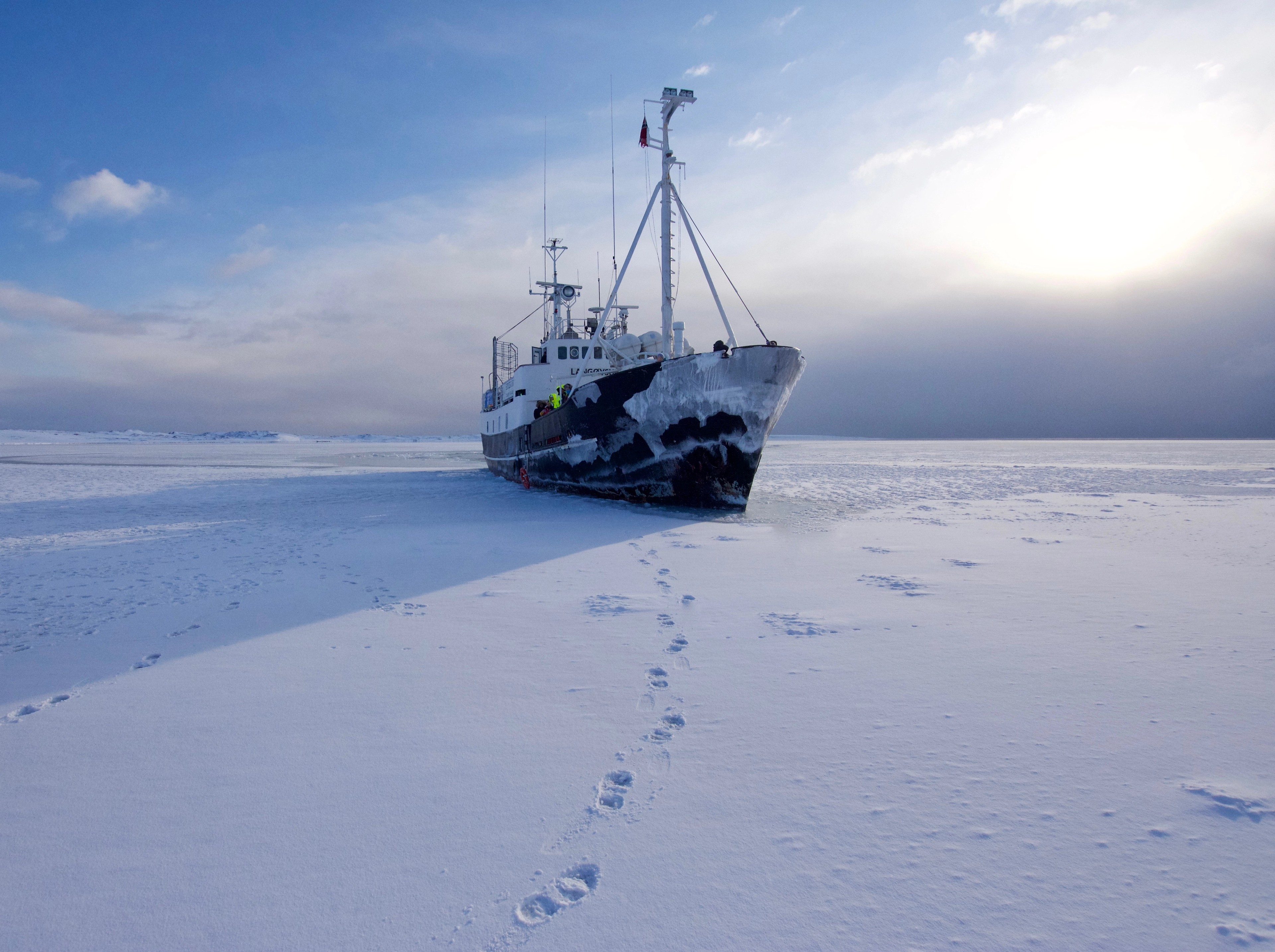 Footprints lead across a snowfield toward a stranded ship.