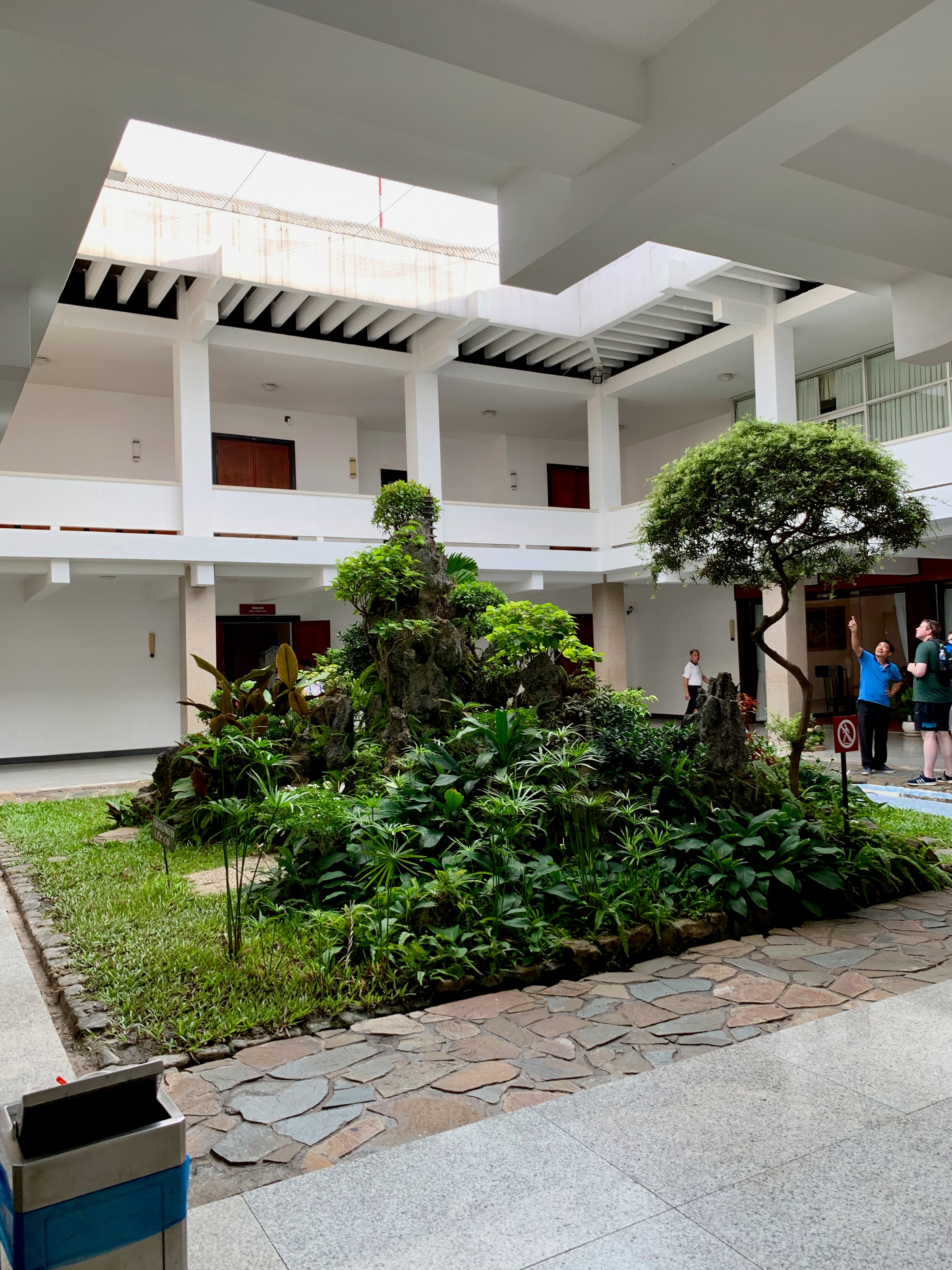 A bright white courtyard building is framed by trees and tropical plants.