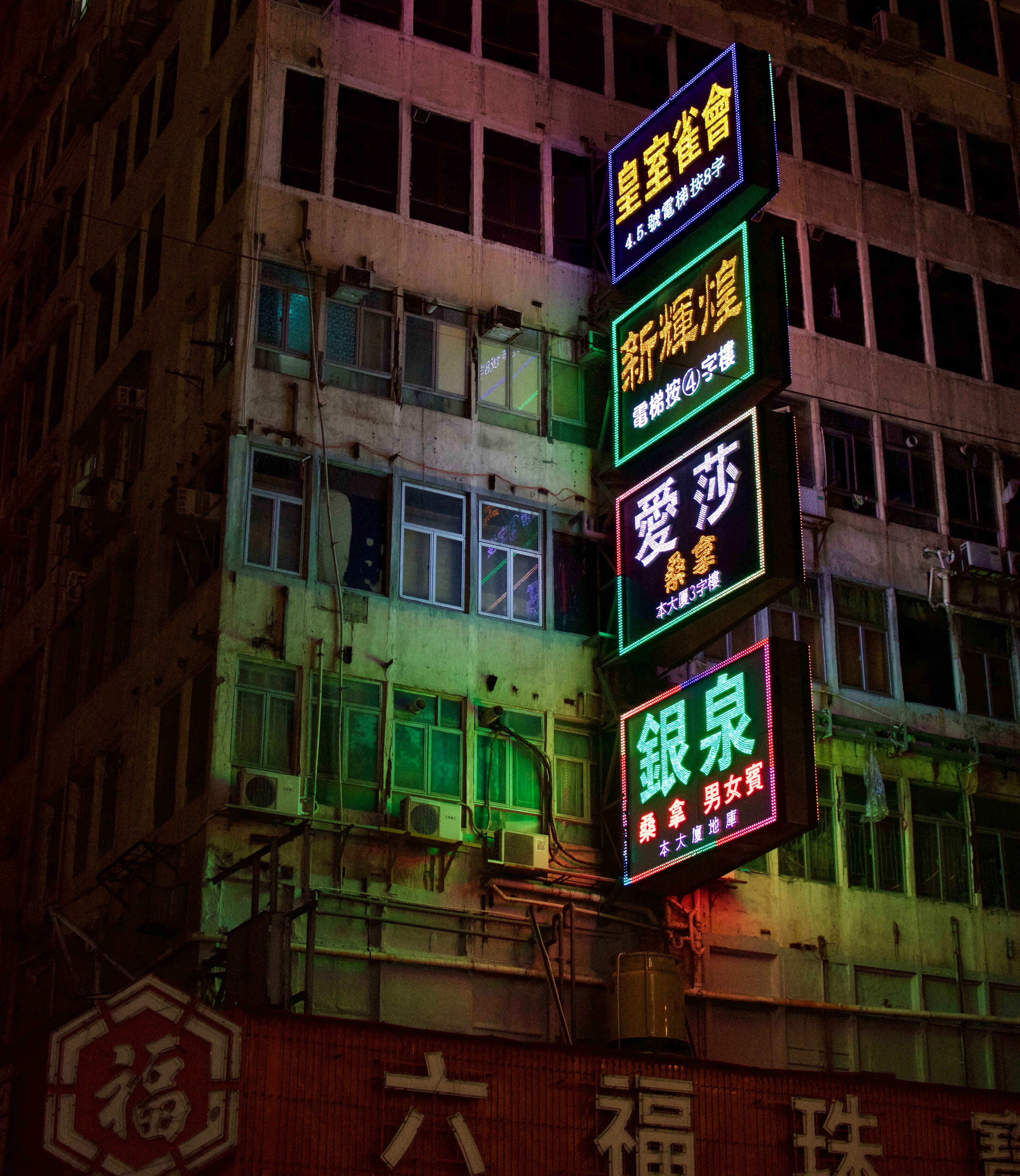 A column of colorful vertical signs is mounted on an apartment building at night.
