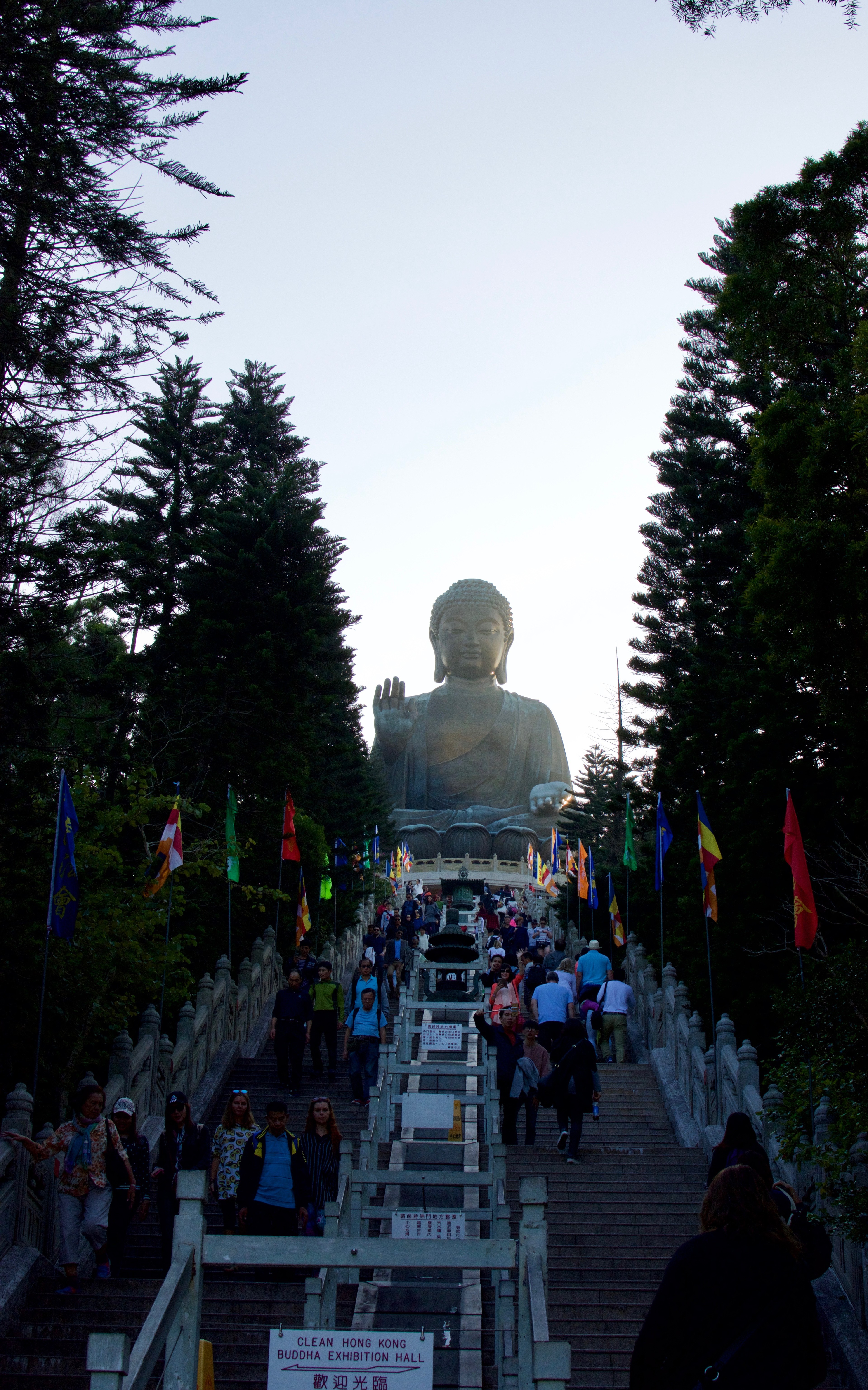 Visitors walk along a tree-lined path toward a large statue.