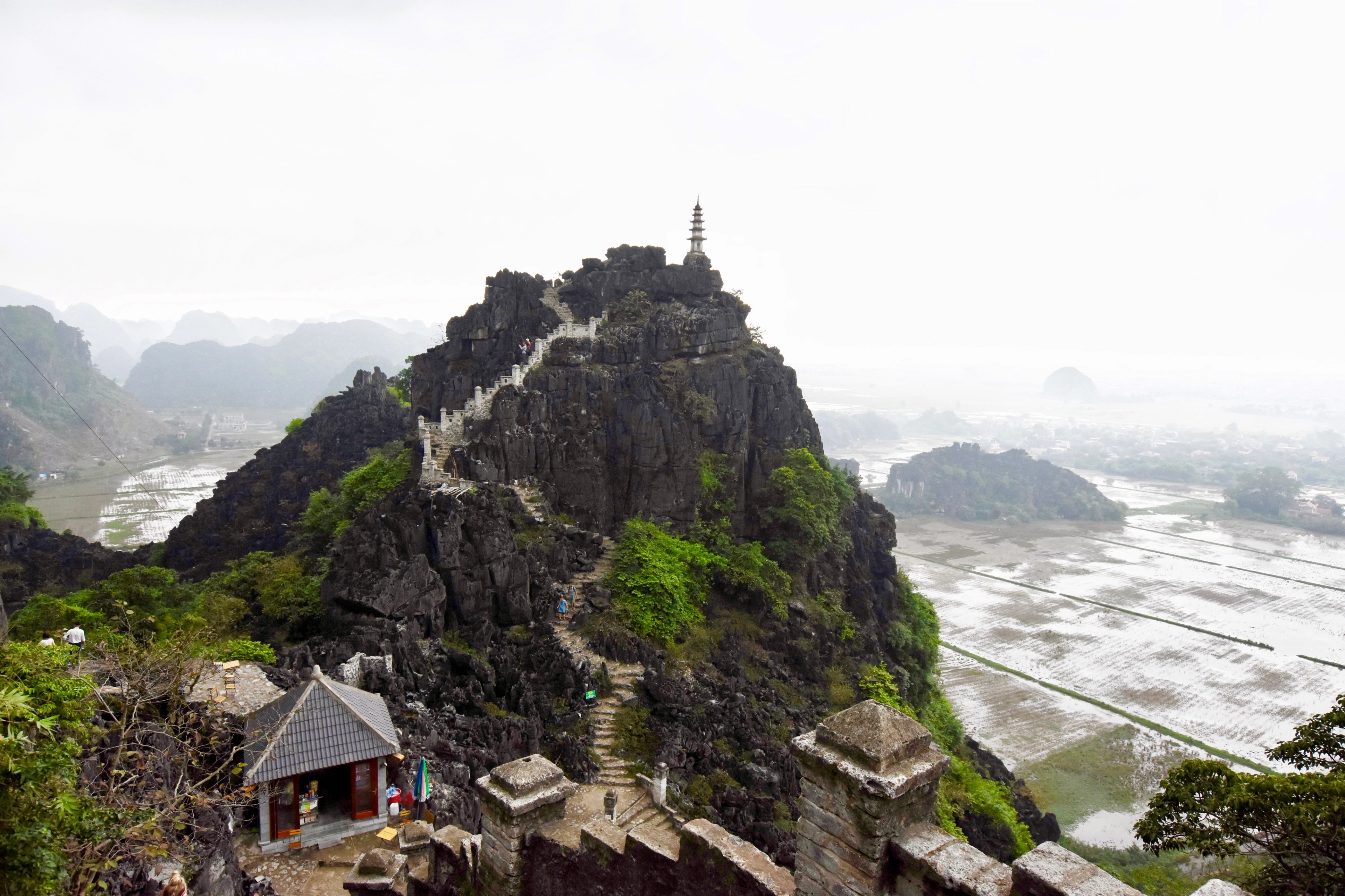 A stone pagoda rises from a rocky hilltop above a hazy landscape.
