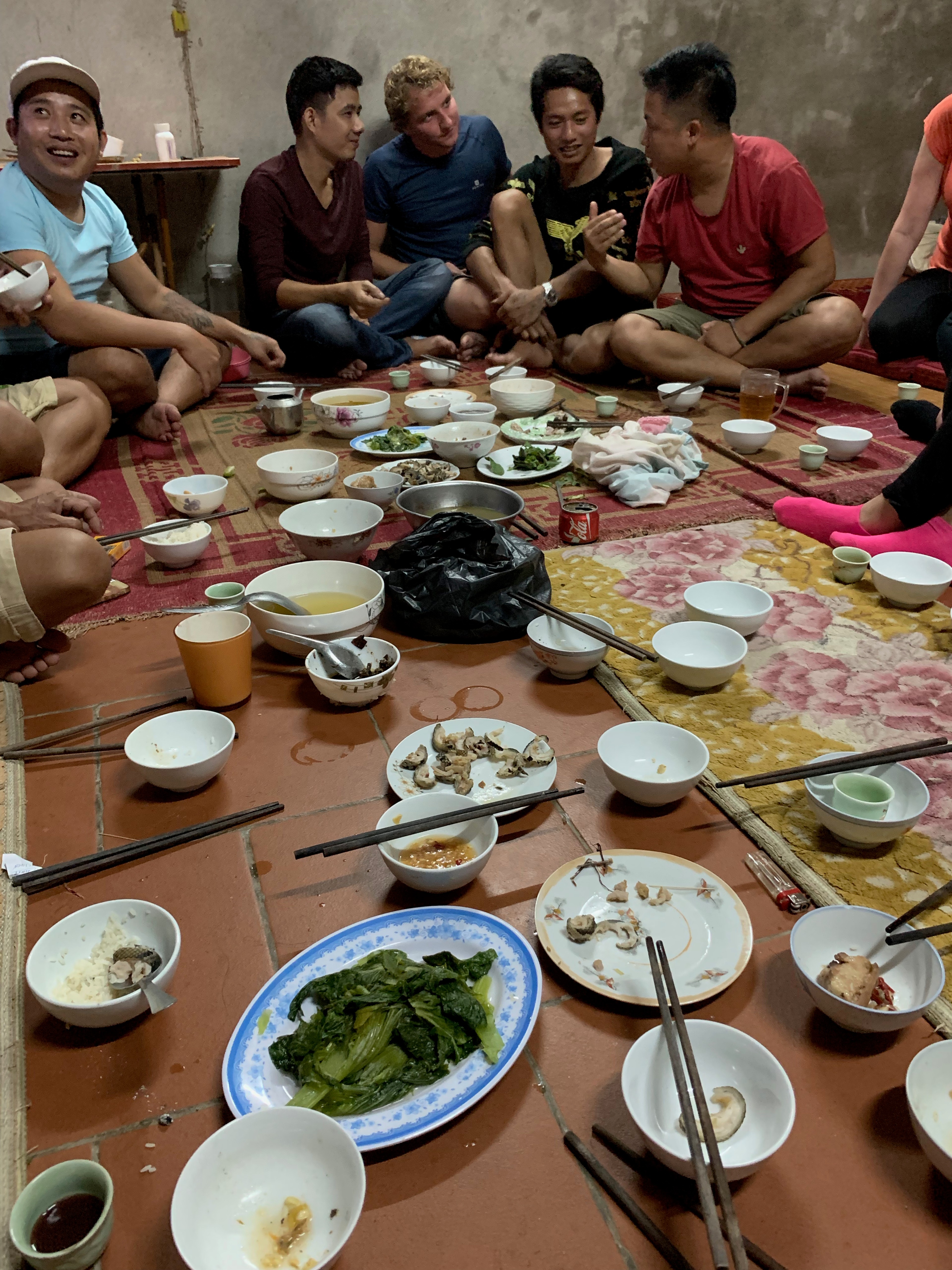 Several people gather around a low table set with a shared meal.