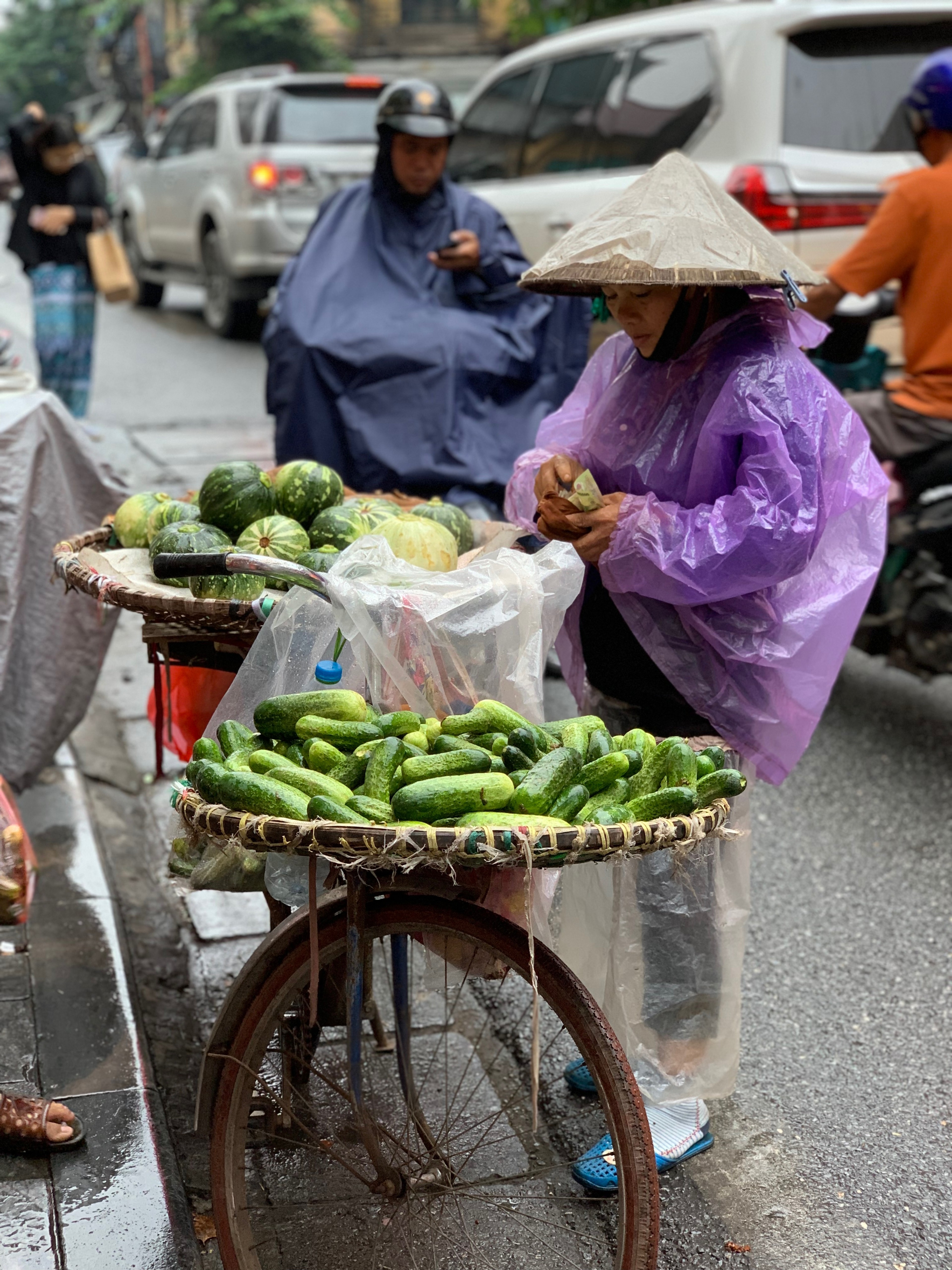 Two vendors display vegetables from bicycles along a city curb.