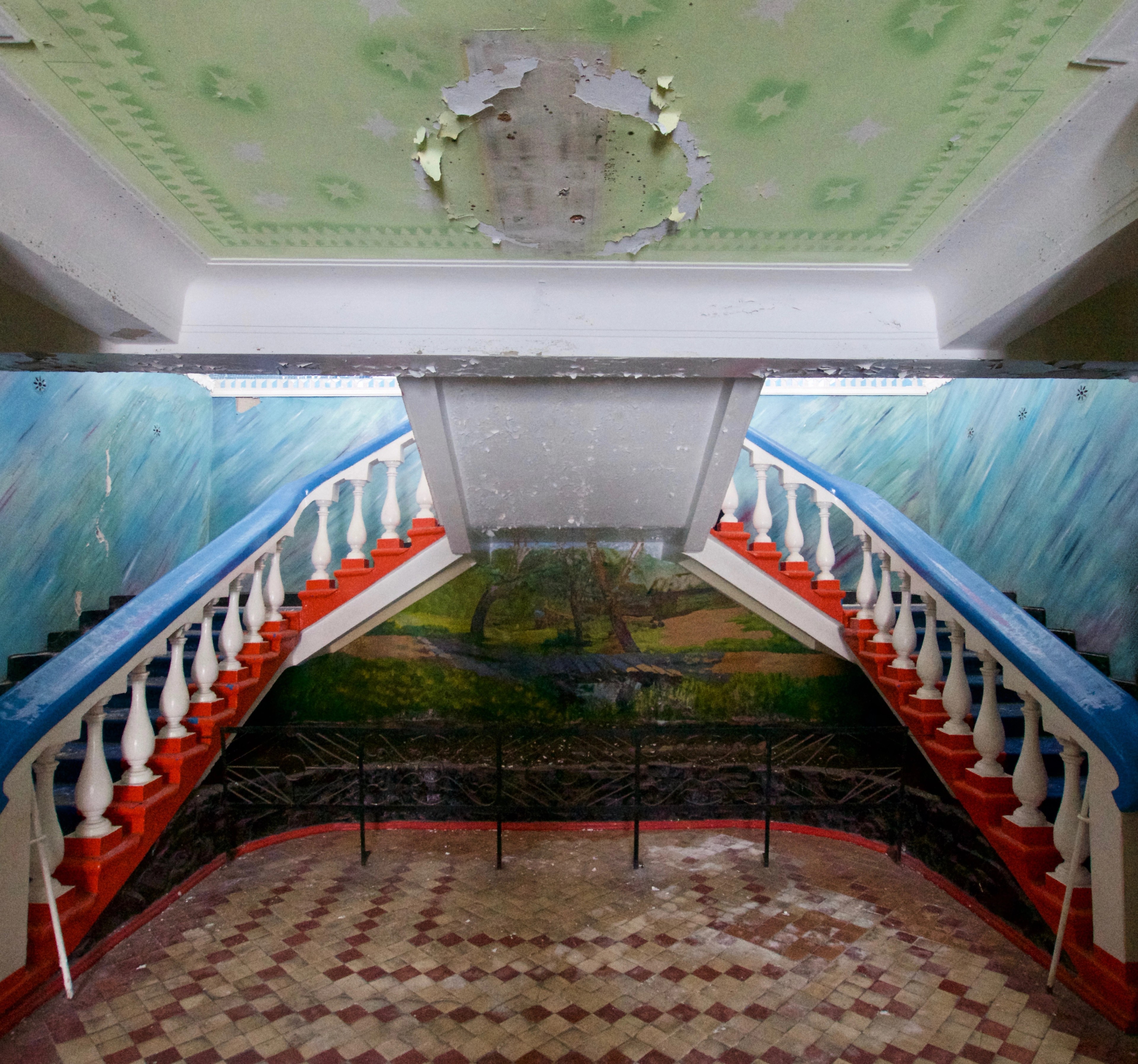 A symmetrical interior stairway descends beneath a painted ceiling.