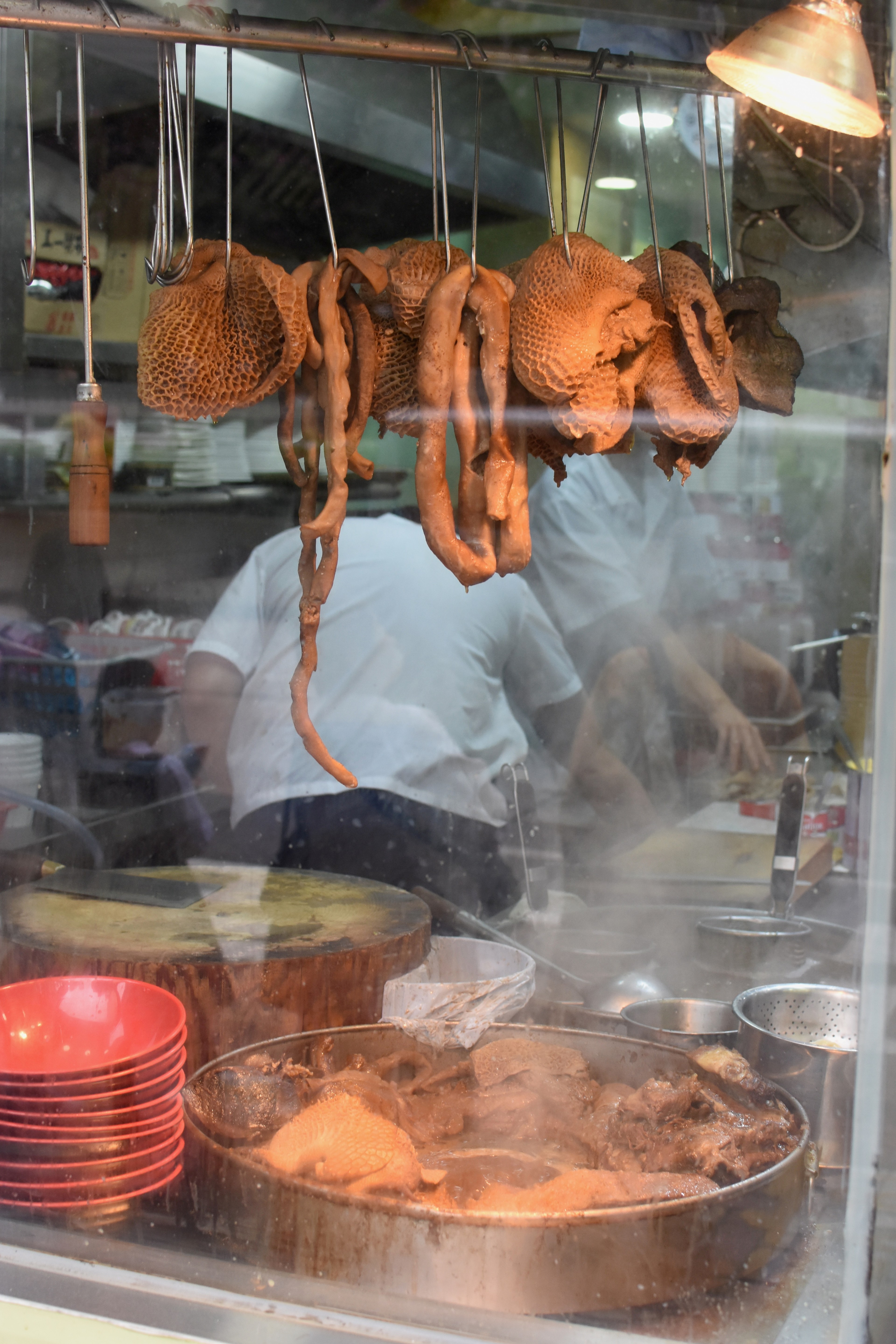 Roasted poultry hangs behind glass in a shop window.