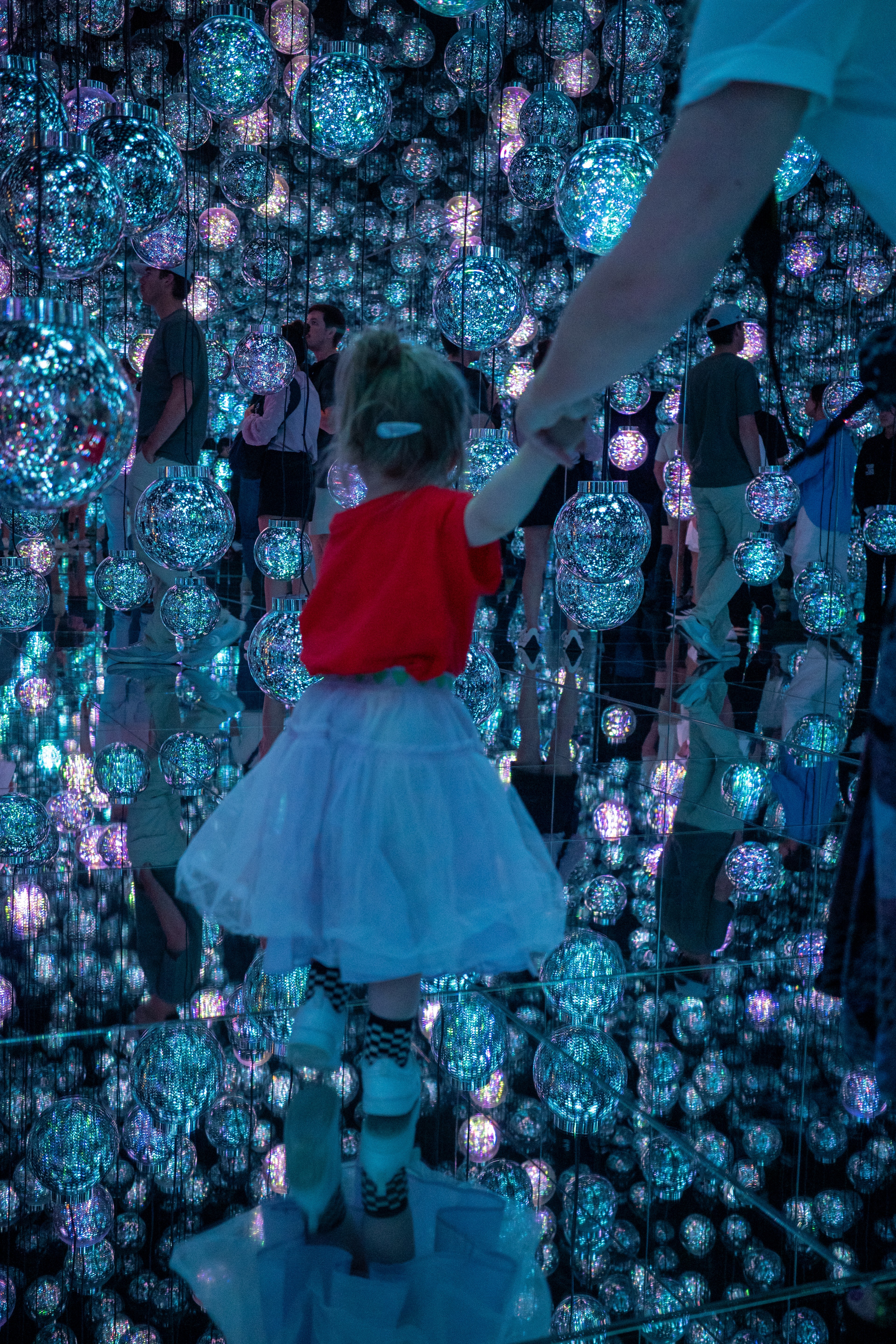 A child in red looks at a colorful immersive art installation.