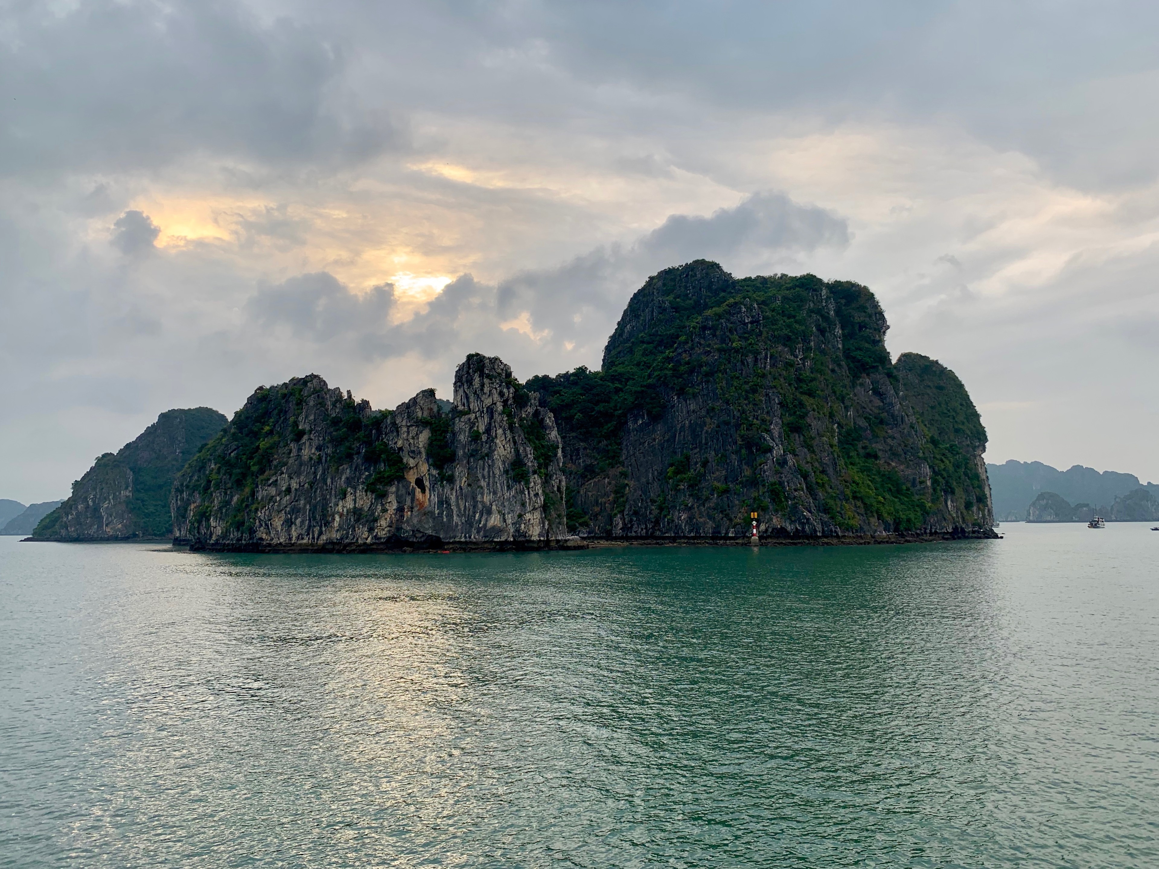 A steep green limestone island rises from the water beneath a cloudy sunset sky.