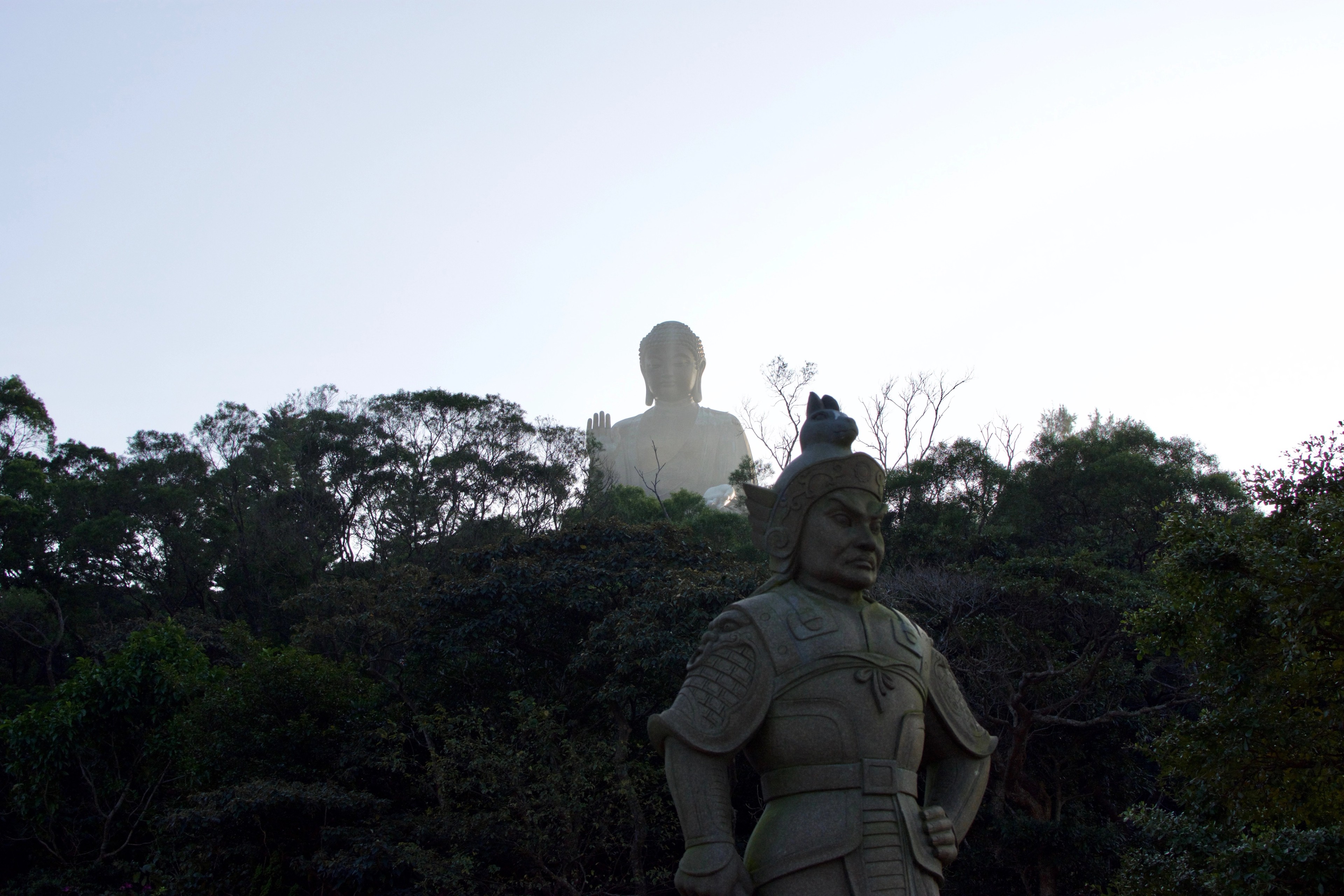 A seated statue is silhouetted among trees on a hillside.