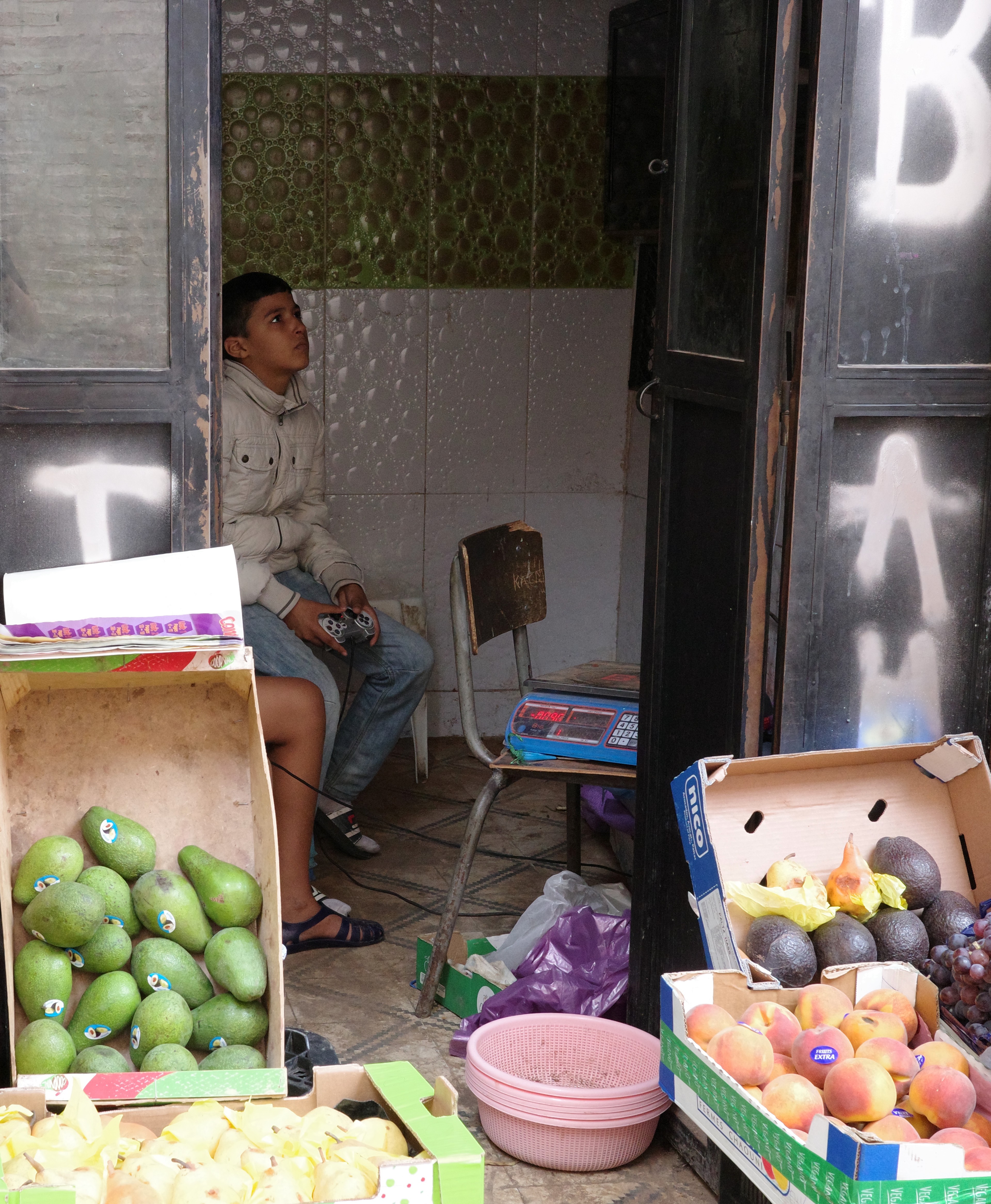A market stall displays green fruit as people gather around it.