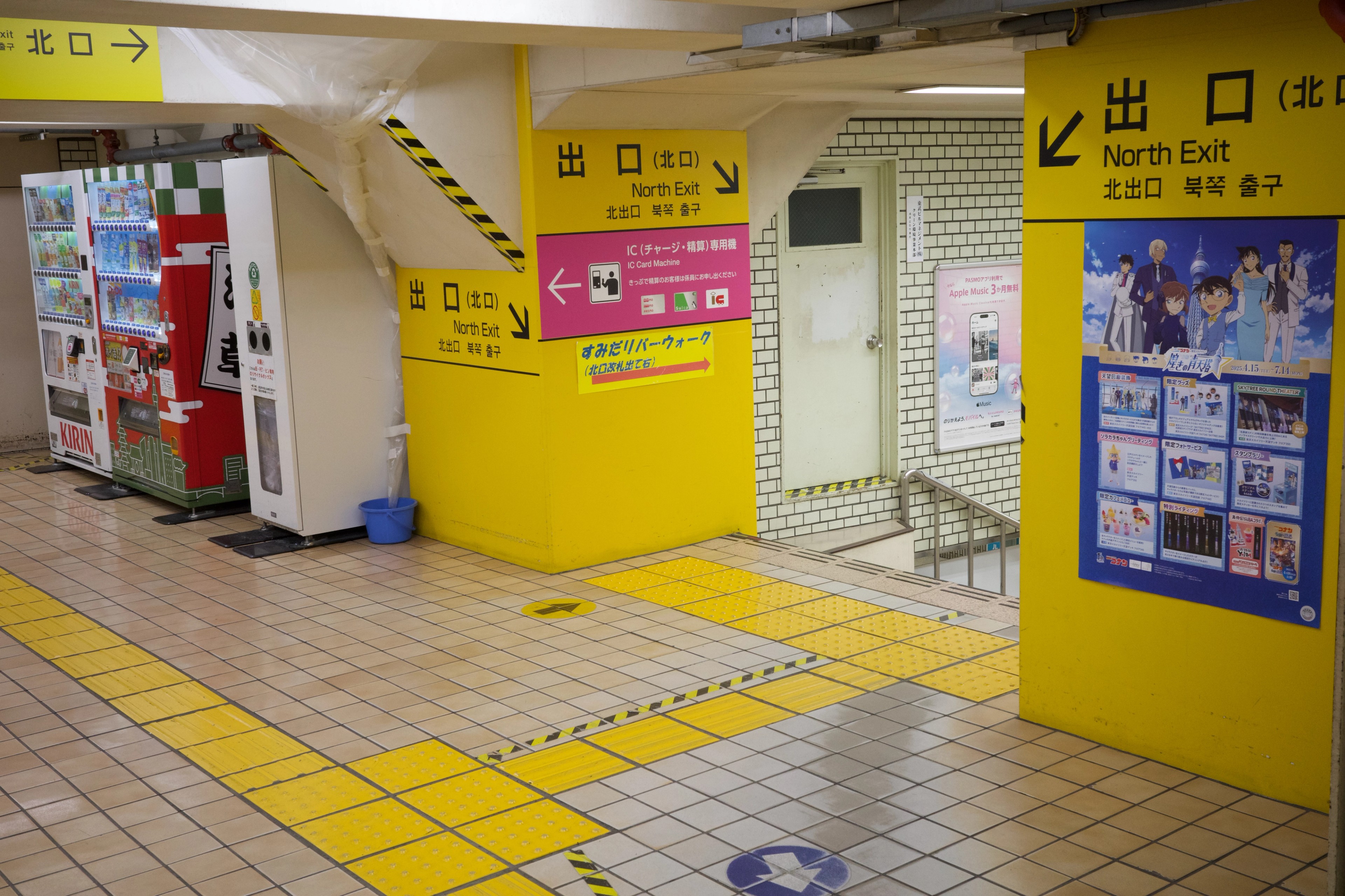 A yellow-walled station corridor with signs and vending machines.