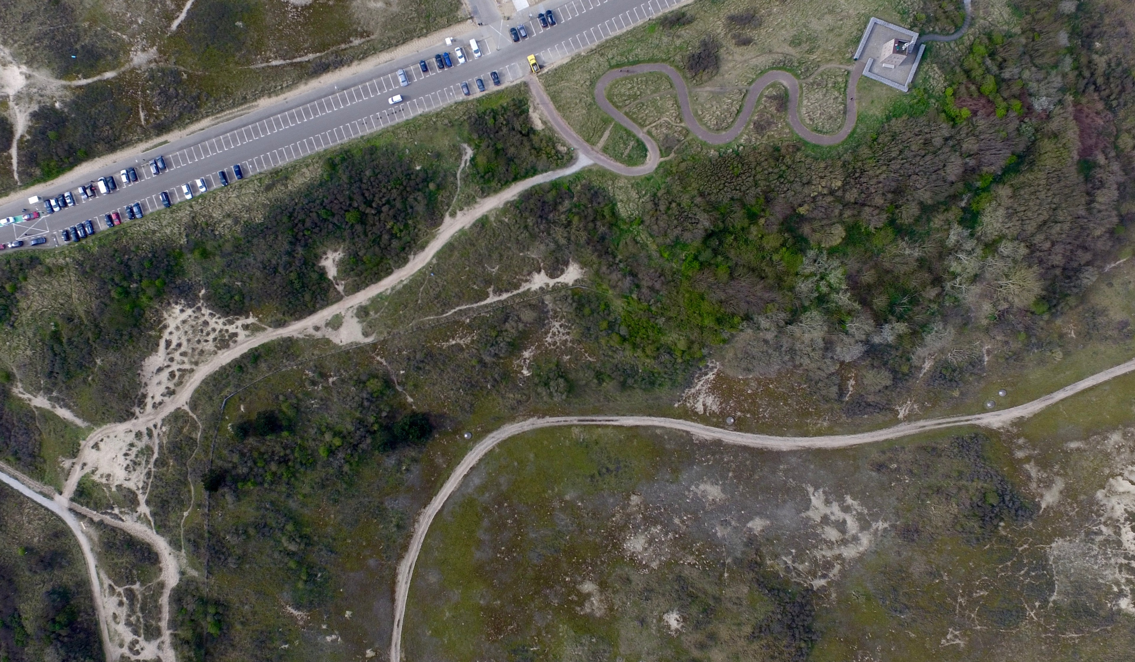 A winding road cuts through scrub and trees beside a larger road.