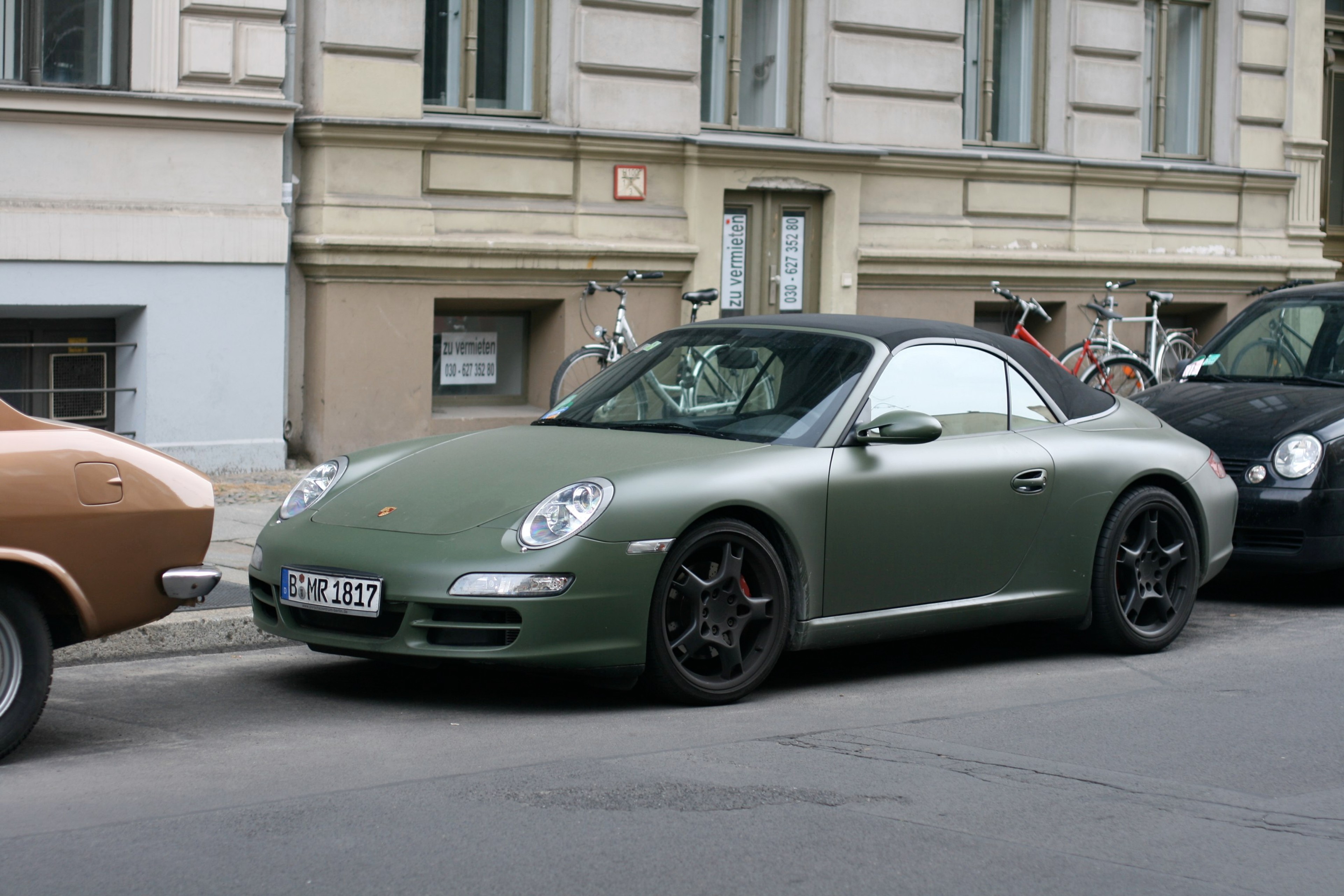 A green sports car is parked at the curb in front of an older city building.