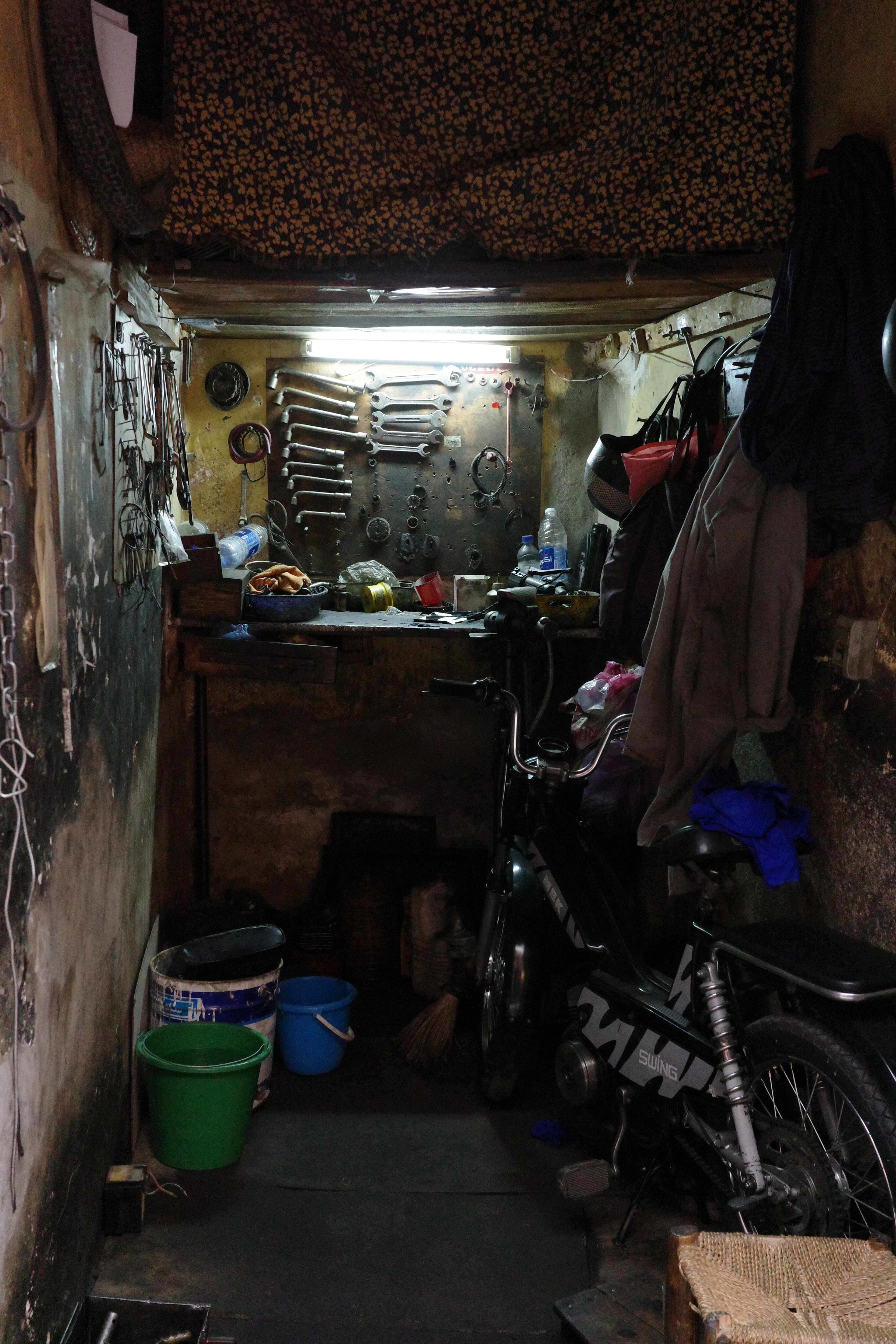 A dim covered passage is crowded with buckets, containers, and market goods.