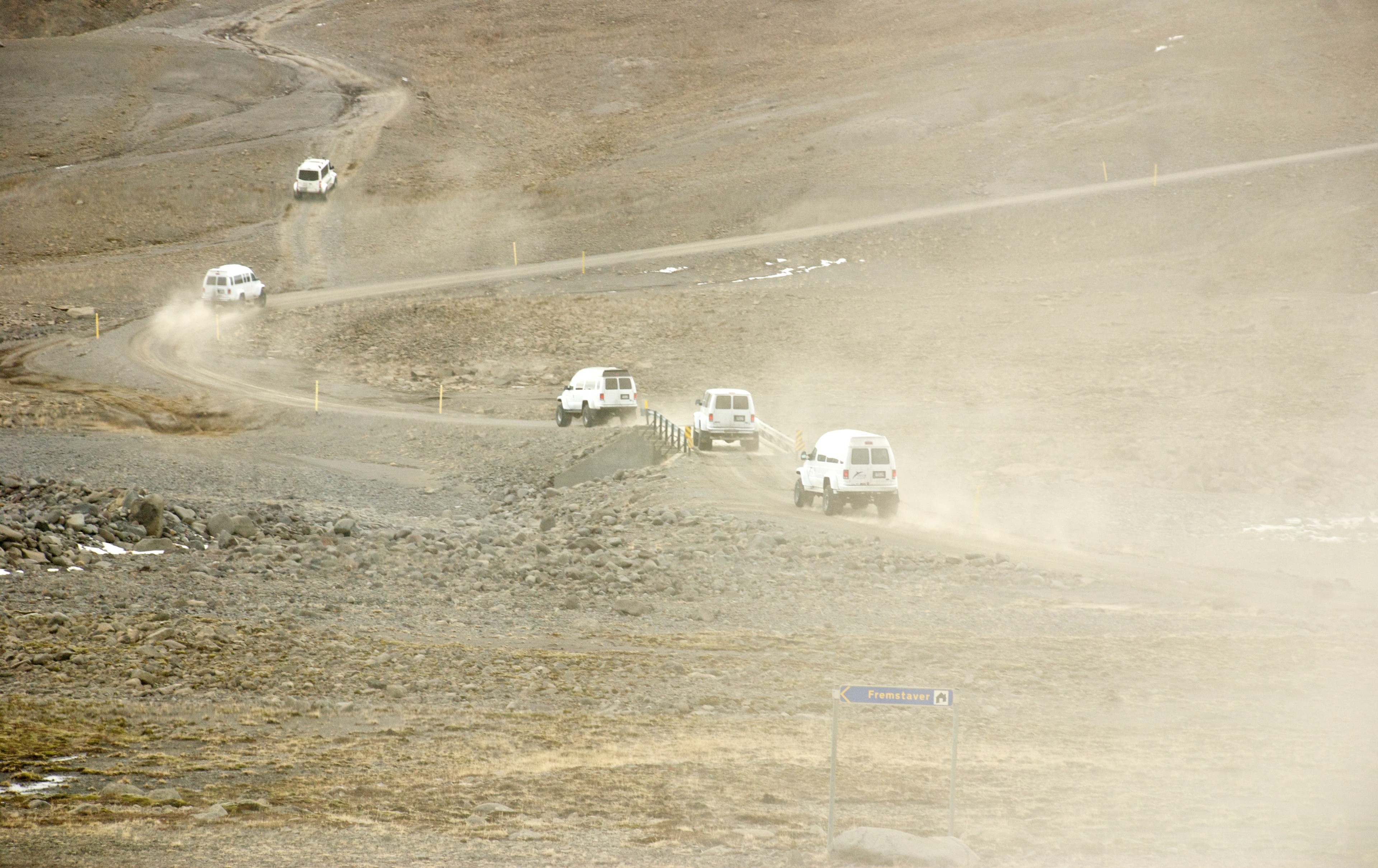 Several vehicles cross a dusty highland plain, viewed from above.