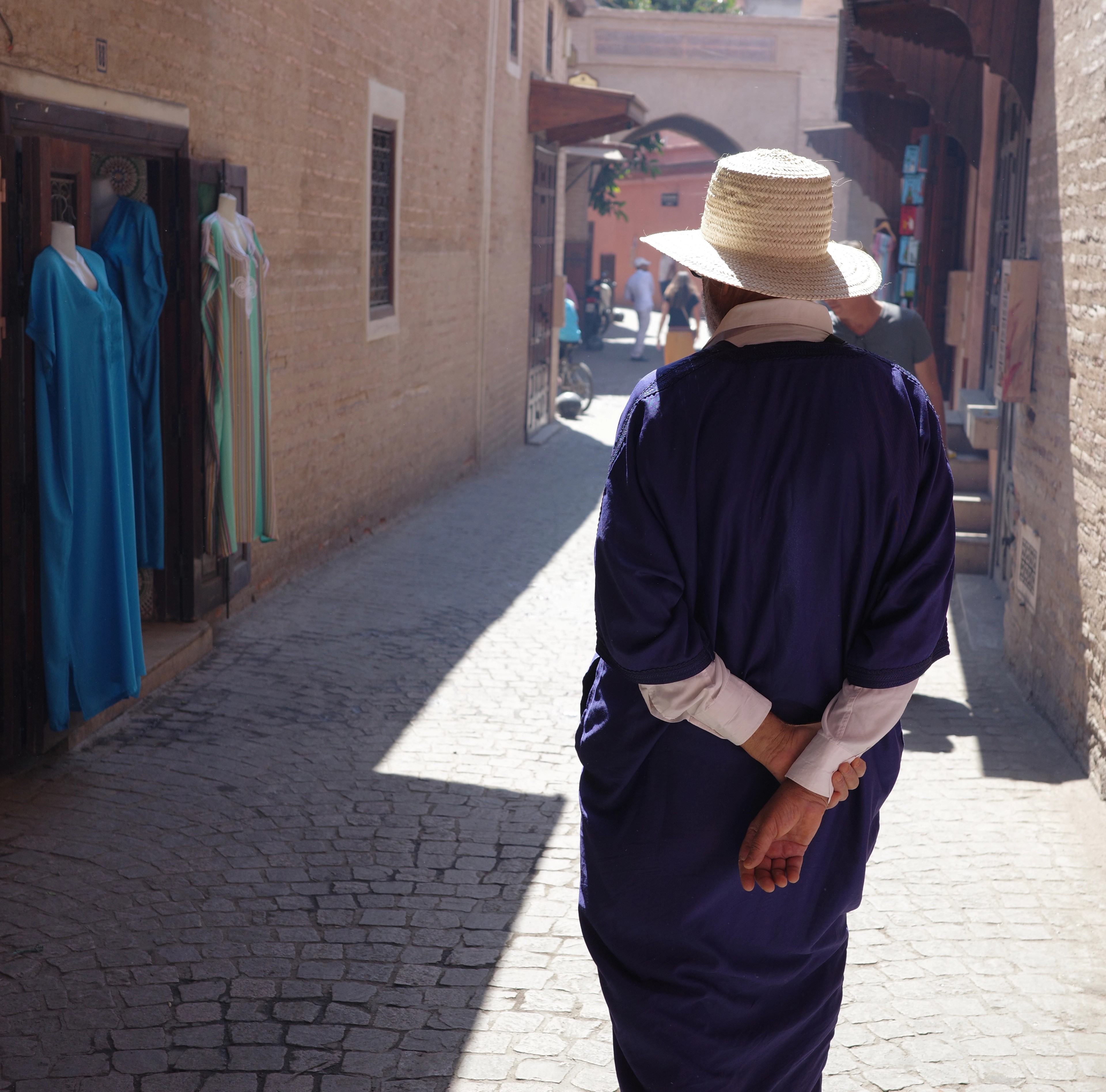 A person wearing a broad straw hat walks away down a narrow alley.