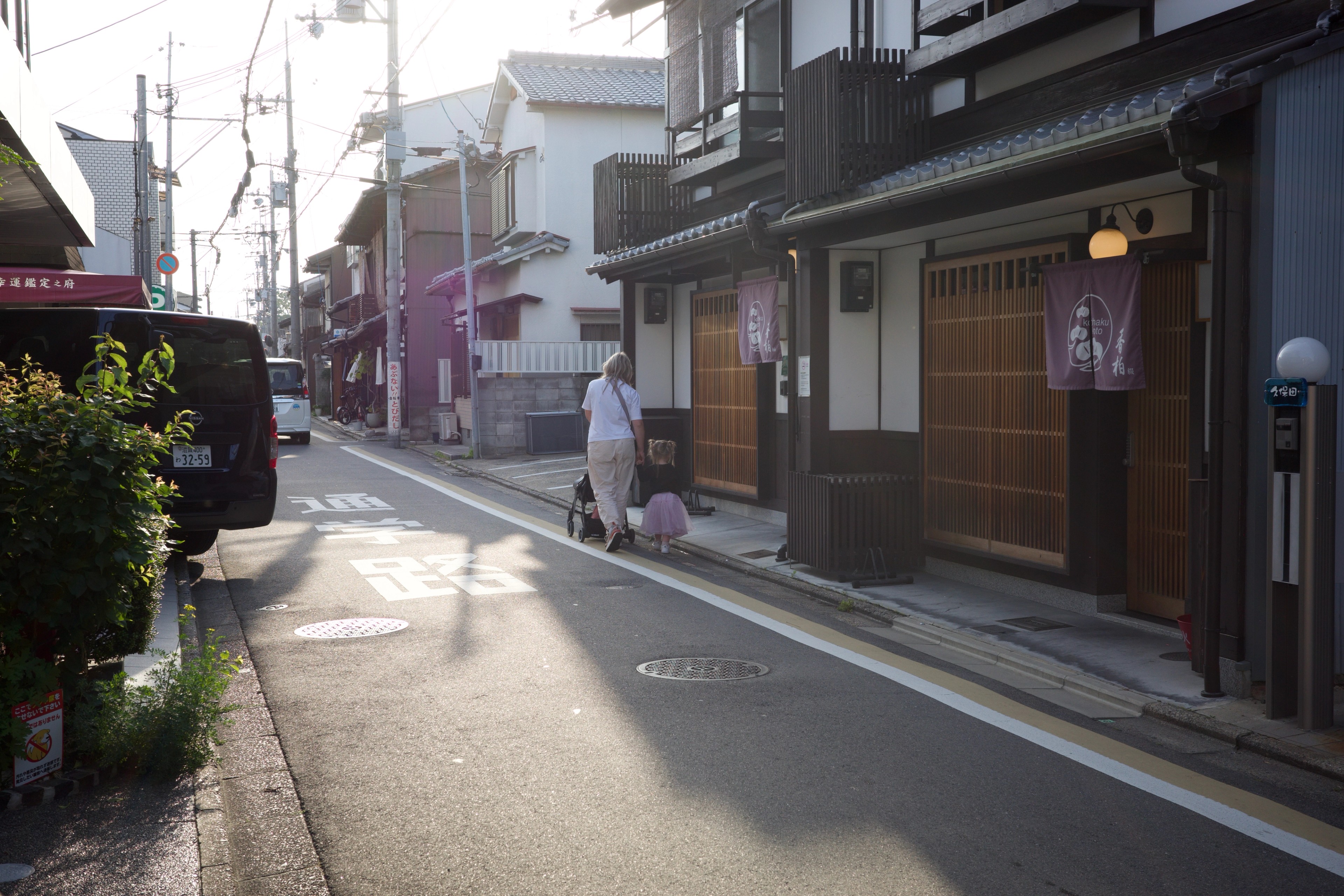 A sunlit lane passes traditional shops and homes.