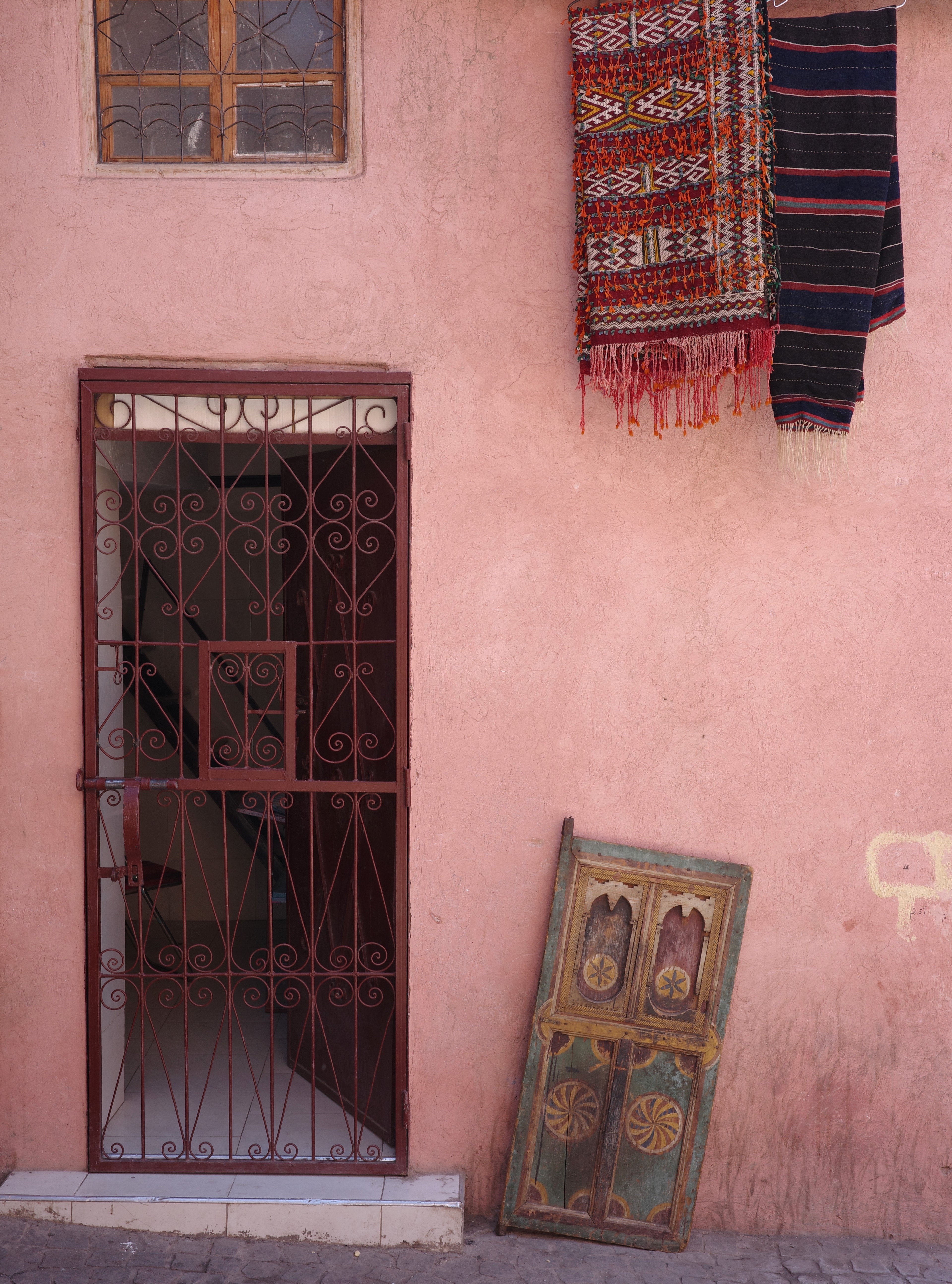 A barred doorway and framed artwork stand against a faded pink wall.